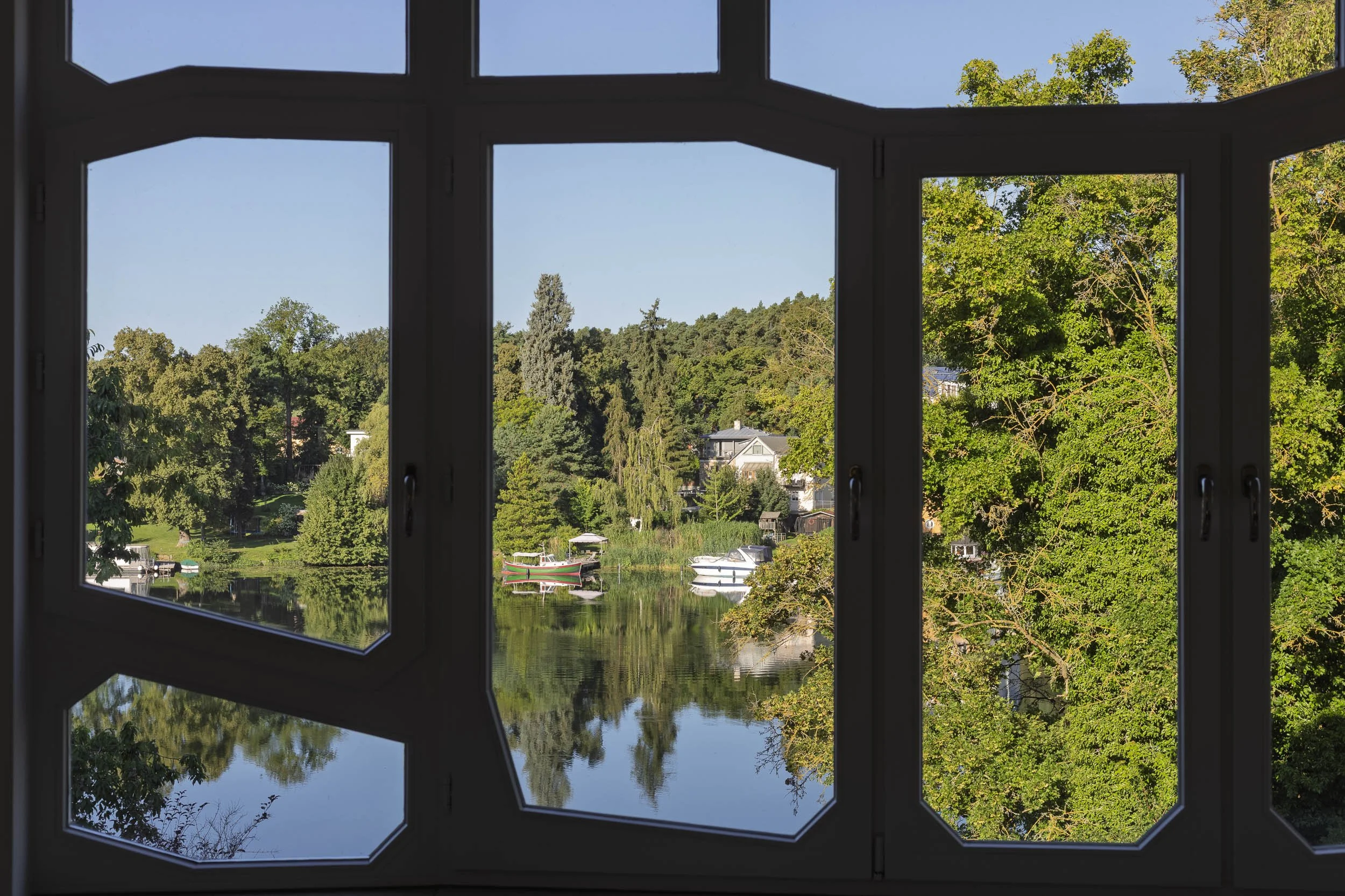 Blick durch große Fenster auf See und grüne Uferlandschaft.