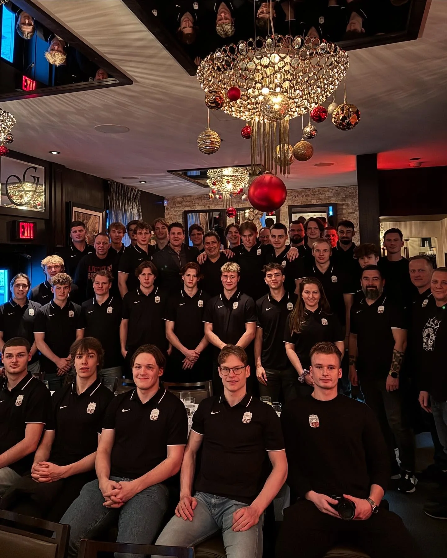Large private party group in matching uniforms gathered at an elegant Ottawa restaurant decorated with holiday chandeliers—perfect venue for group events and private parties.