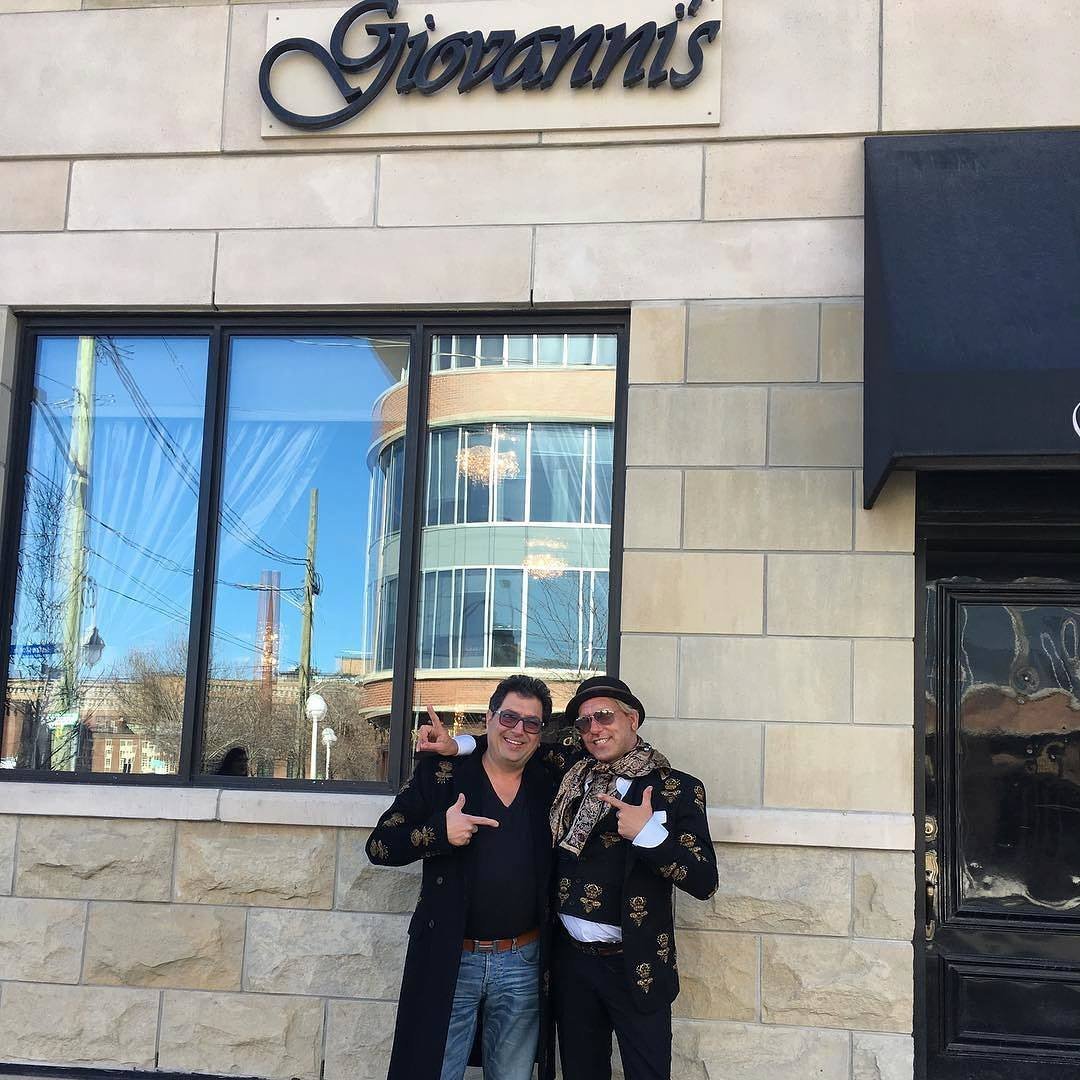 Two smiling men pose in front of Giovanni’s, a well-known Italian restaurant in Canada, showcasing the warm hospitality and upscale atmosphere of Italian dining.