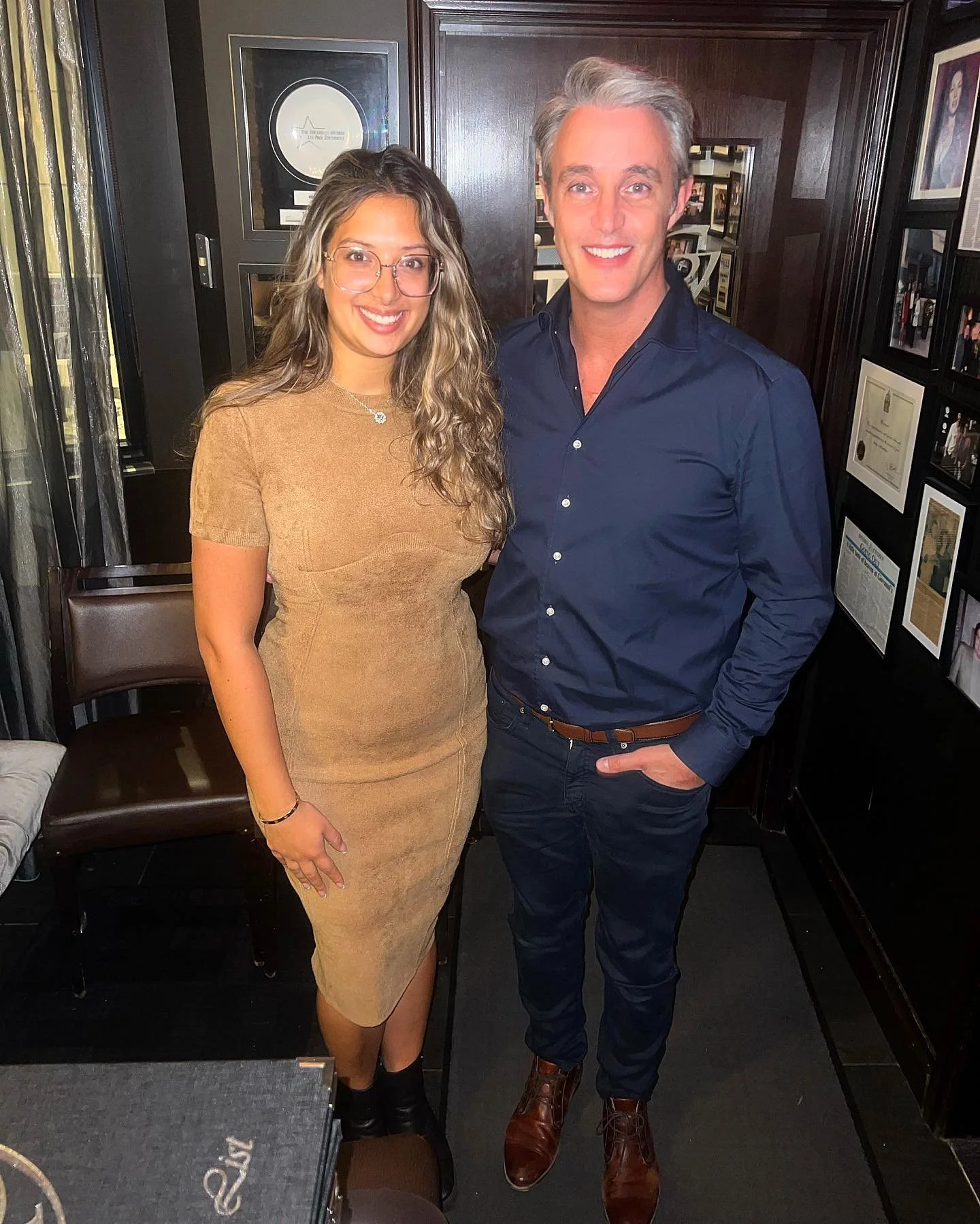 Two guests posing inside a restaurant with private room in Ottawa, surrounded by dark wood paneling, framed awards, and an intimate fine dining ambiance—ideal for exclusive dinners and special occasions.