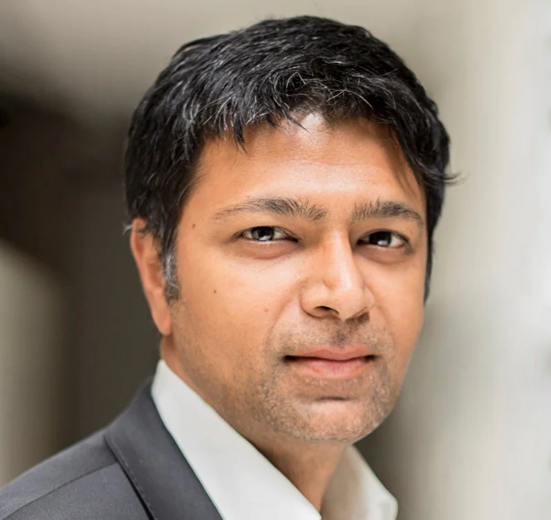 Close-up portrait of a Sriram Subramanian wearing a white shirt and dark suit jacket, looking into the camera.