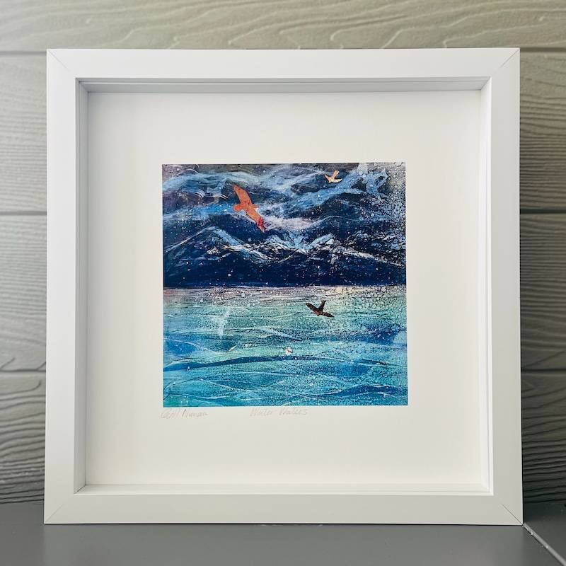 white box framed print of snowy mountain peaks on a wintery day with seabirds wheeling over the sea - shades of blues with orange collaged bird shapes