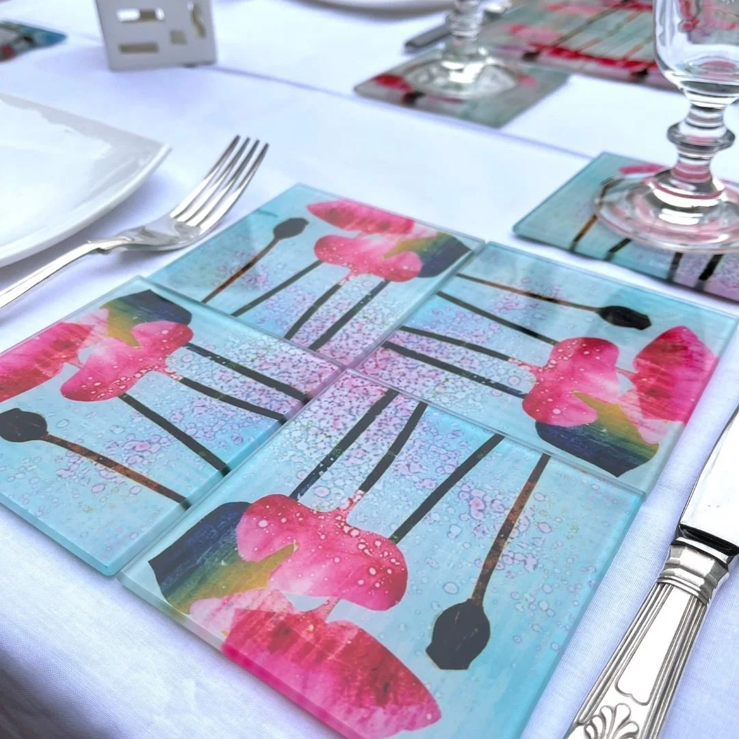 a place setting of 5 coasters, 4 for the plate and 1 for a wine glass in a dinner table setting featuring pink poppies and tulip against a sky blue background with splashes