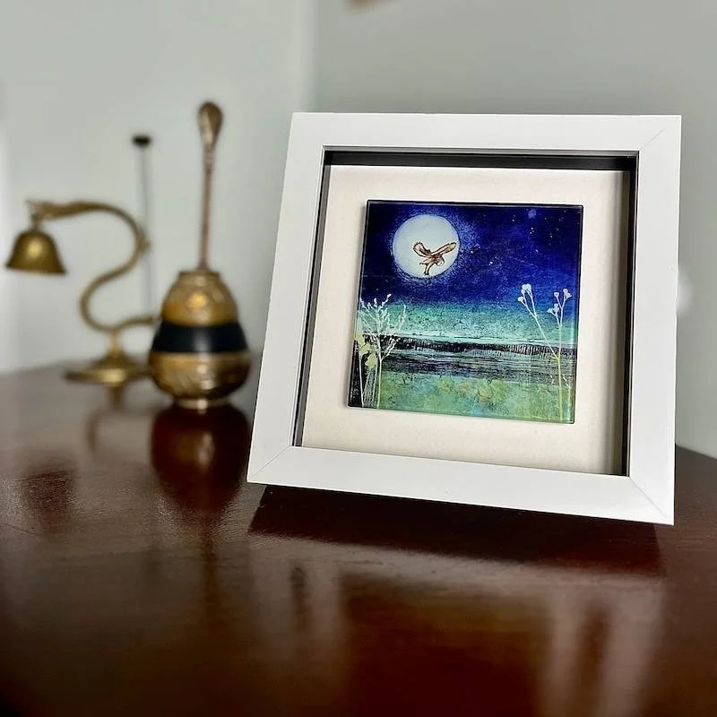 glass art tile - on the hunt - a collagraph print featuring an owl hovering up over a moorland landscape under a full moon framed in a white box frame on a side table