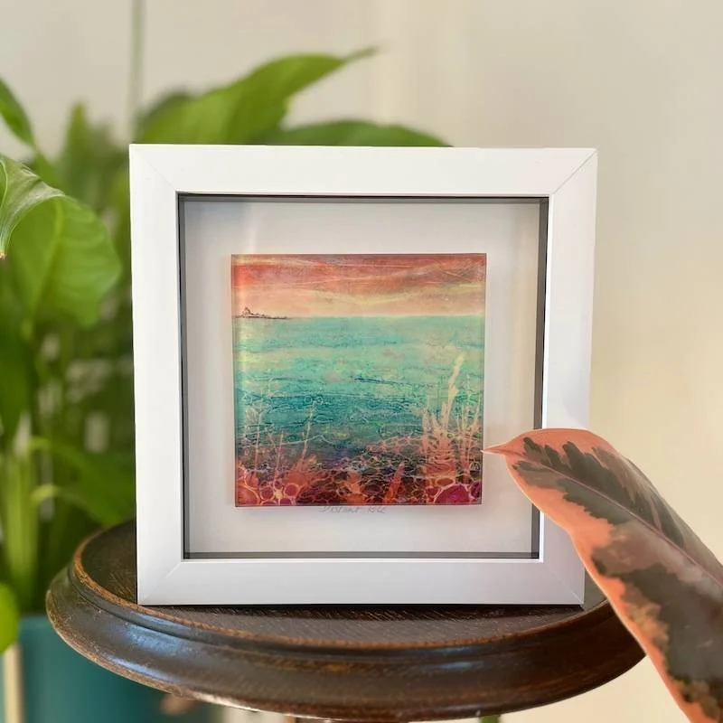 glass-art-tile-carol-nunan-distant-isle glass art tile - on the hunt - a collagraph print  featuring the seascape outlooking over to holy island framed in a white box frame on a shelf