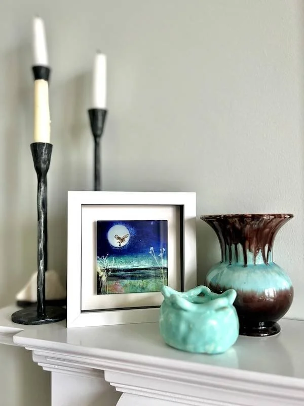 glass art tile - on the hunt - a collagraph print featuring an owl hovering up over a moorland landscape under a full moon framed in a white box frame on a mantelpiece