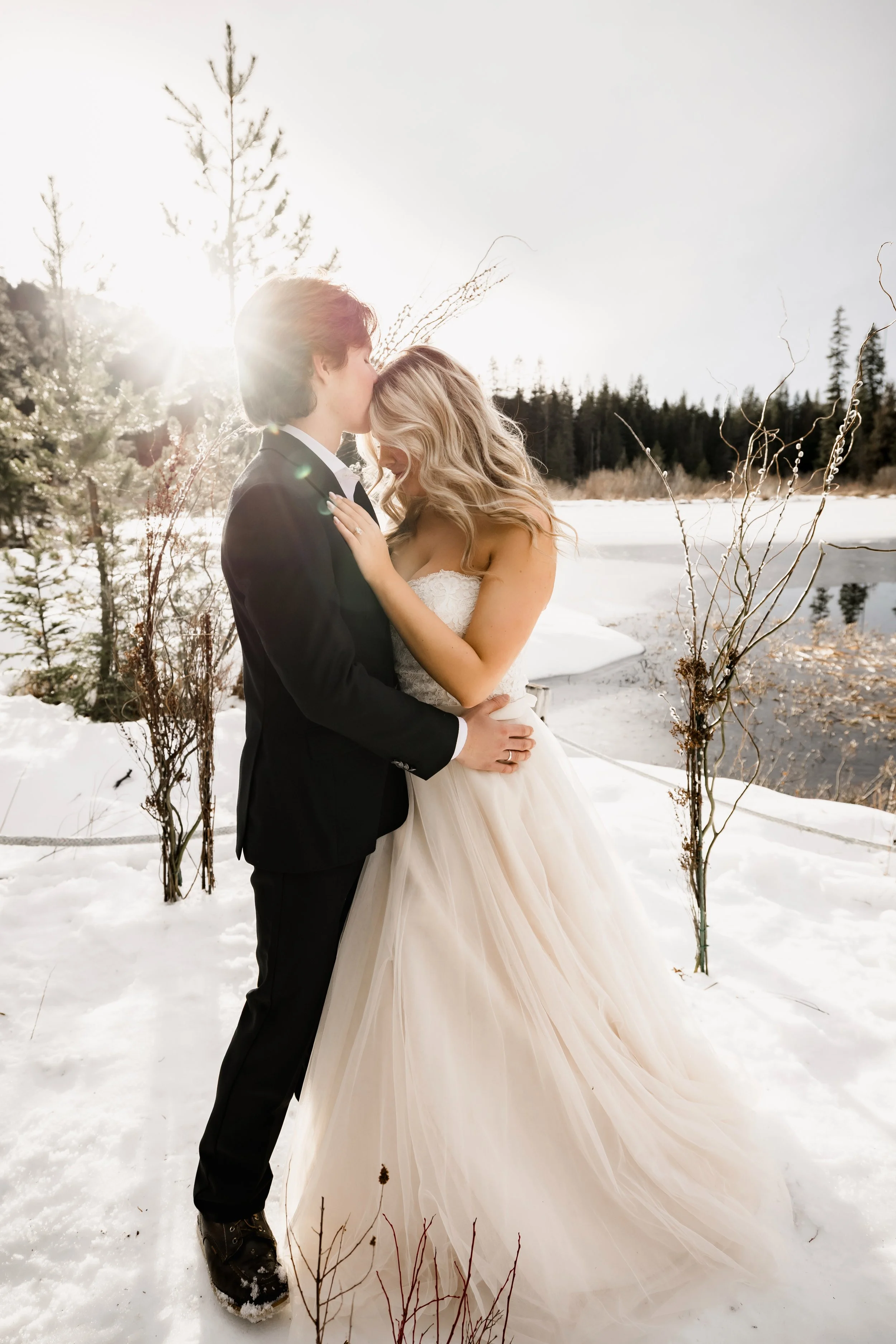 Bride and groom kissing in the winter sun on the snowy shoreline of Trillium Lake near Mt. Hood