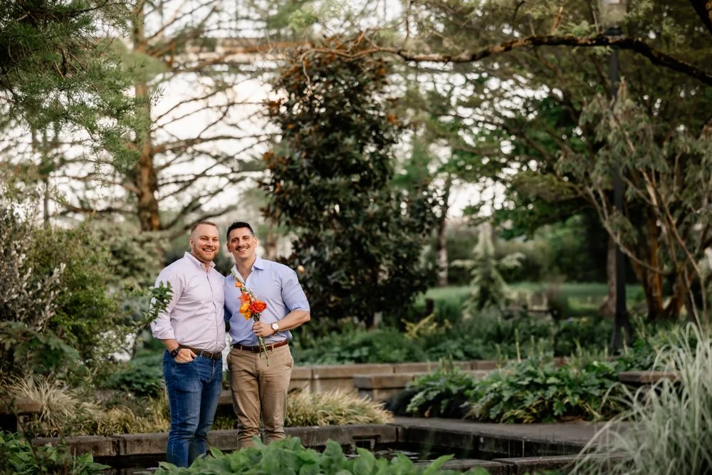 Two grooms holding a vibrant orange and coral bouquet at sunset during their Portland engagement photos