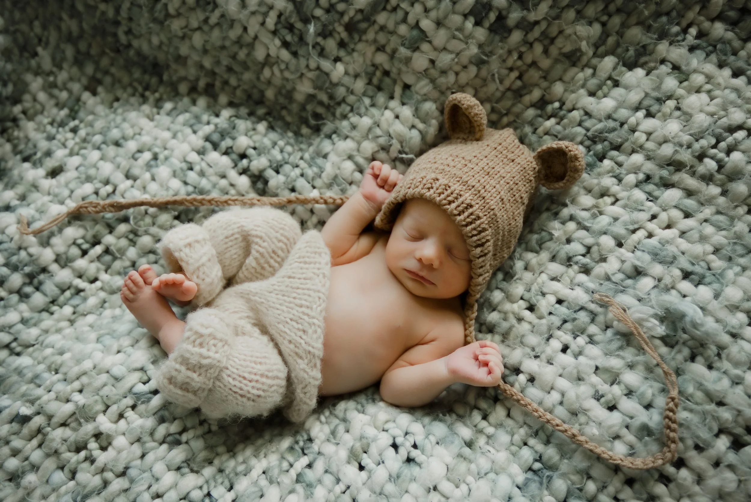 Newborn in a knit bear bonnet asleep on a chunky woven blanket, styled by an Estacada newborn photographer