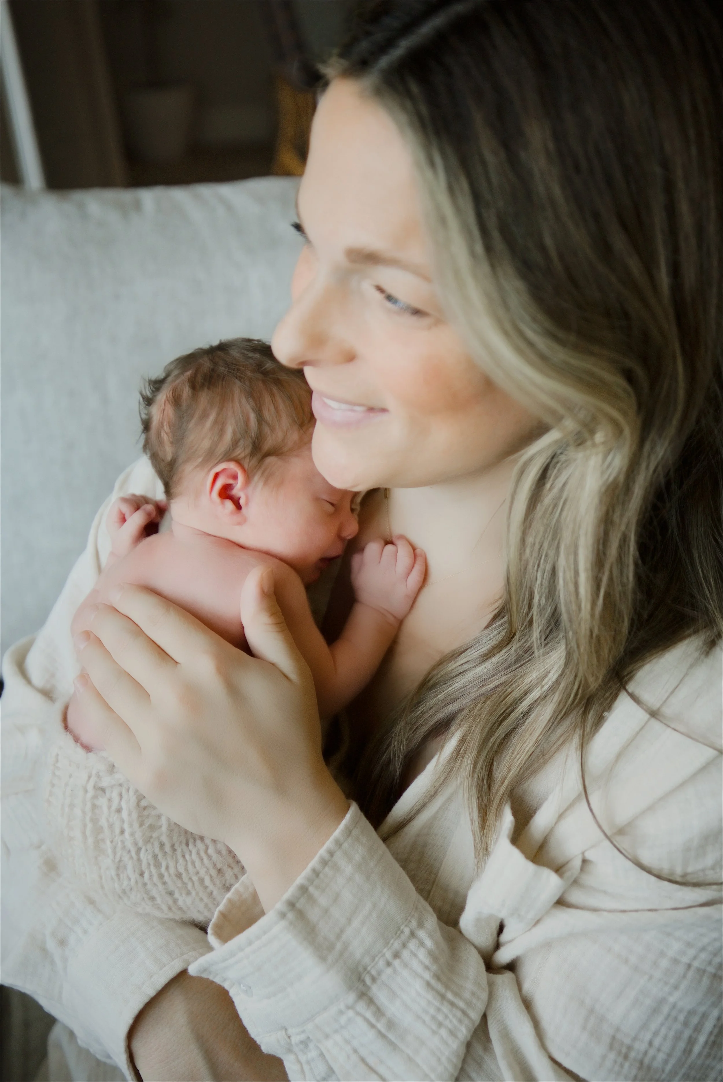 Mom cradles her one week old close, wrapped in soft window light