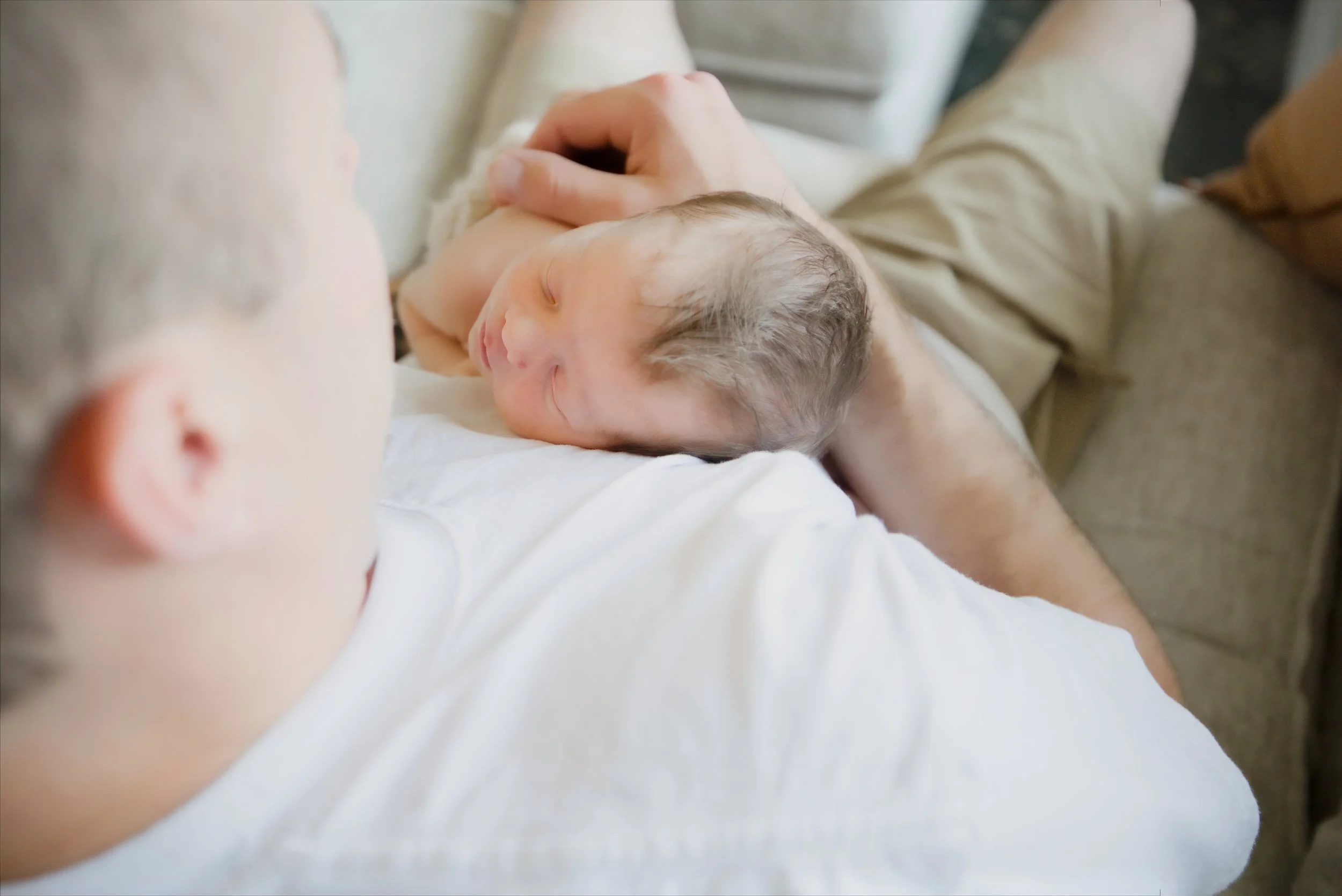 Newborn rests on Dad's shoulder in soft window light