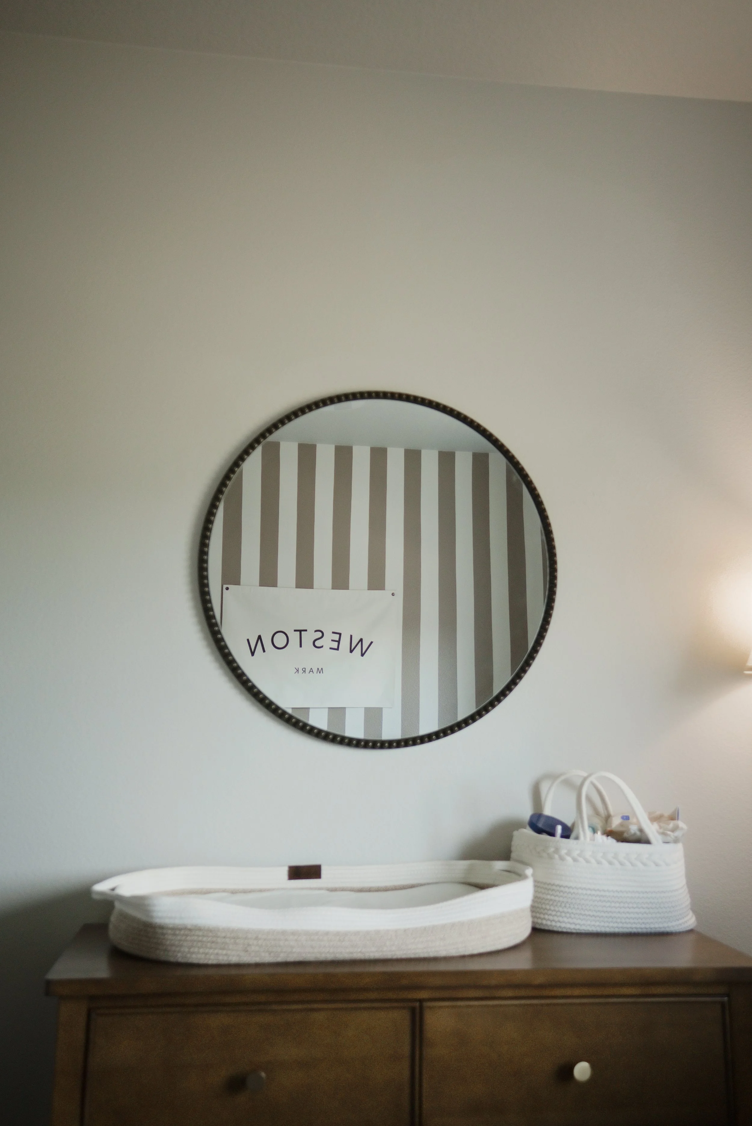 Round mirror above the changing table reflects the striped nursery wall