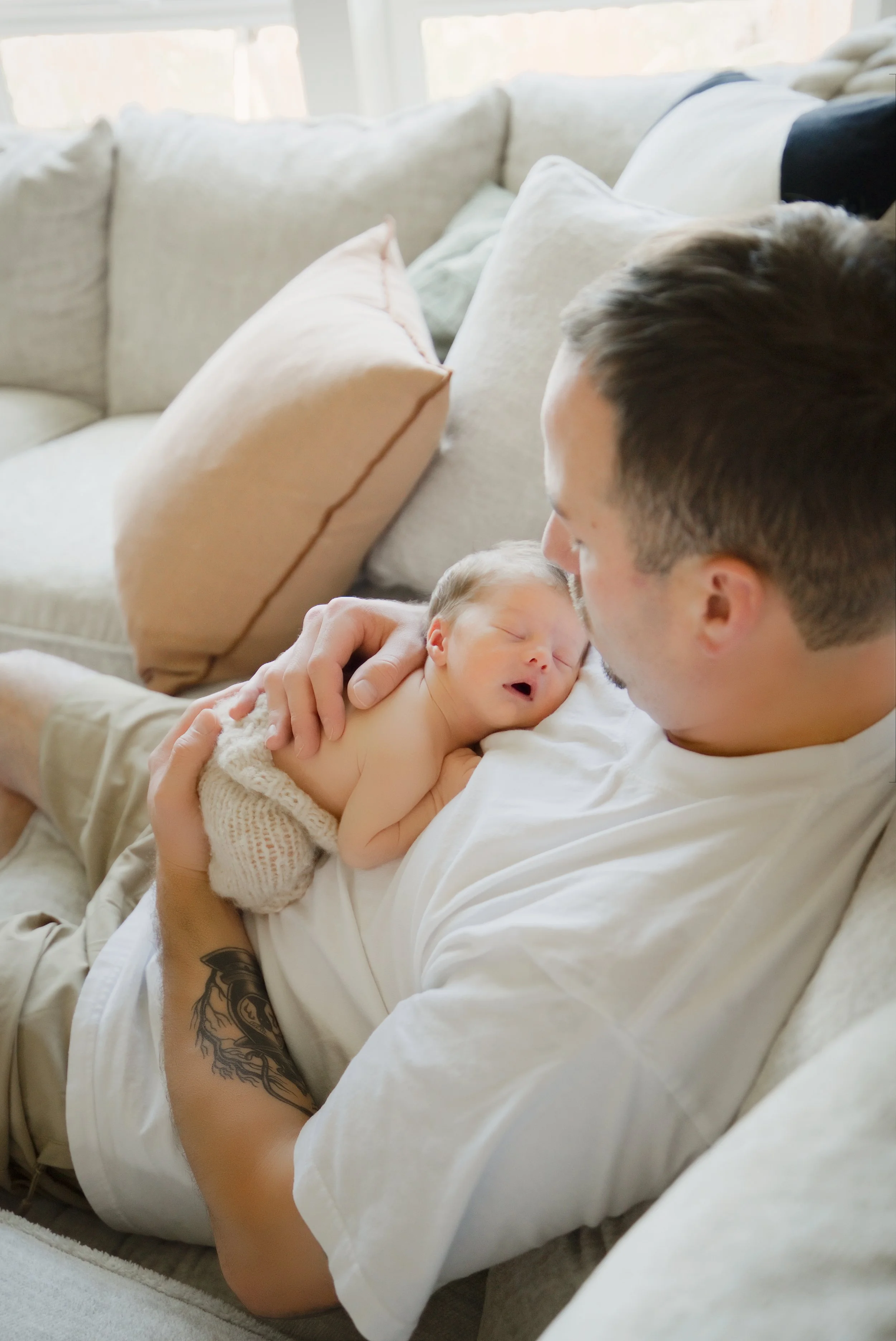 Dad relaxes on the couch with the baby tucked into his arms