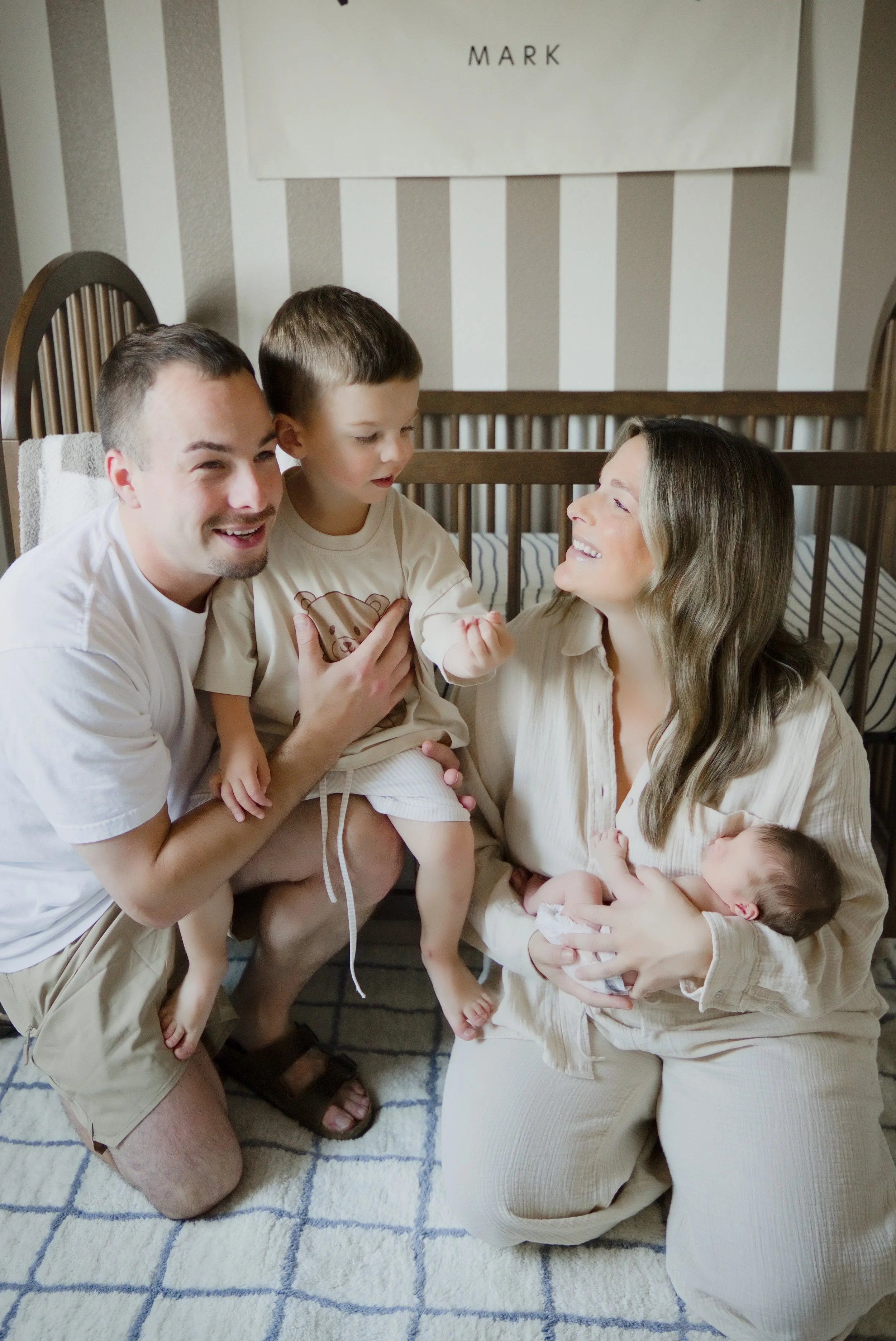 Mom, Dad, and big brother gather around the baby in the striped nursery