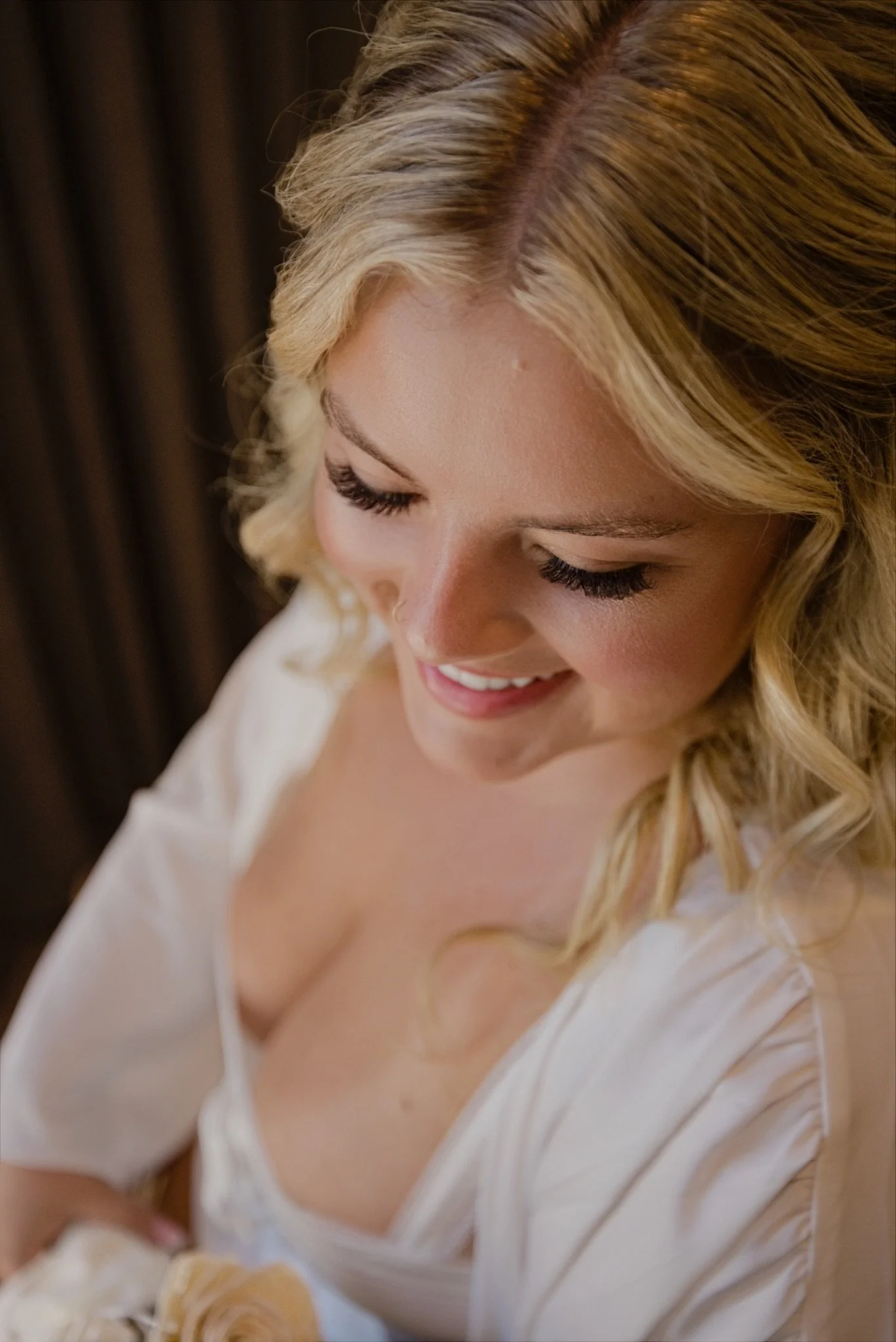Sarah looking at her white bouquet in soft window light