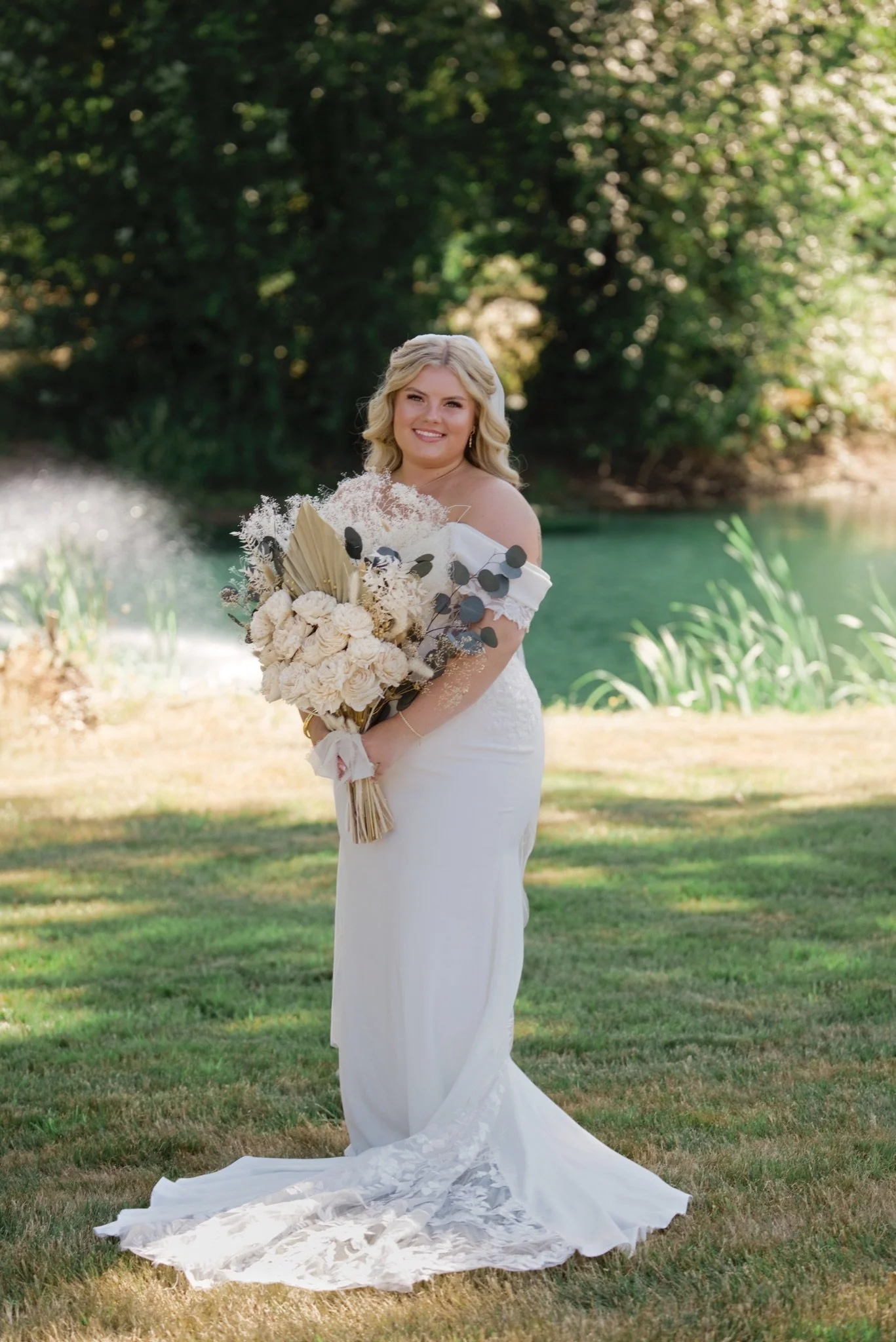 Sarah holding her bouquet on the lawn in front of the trees