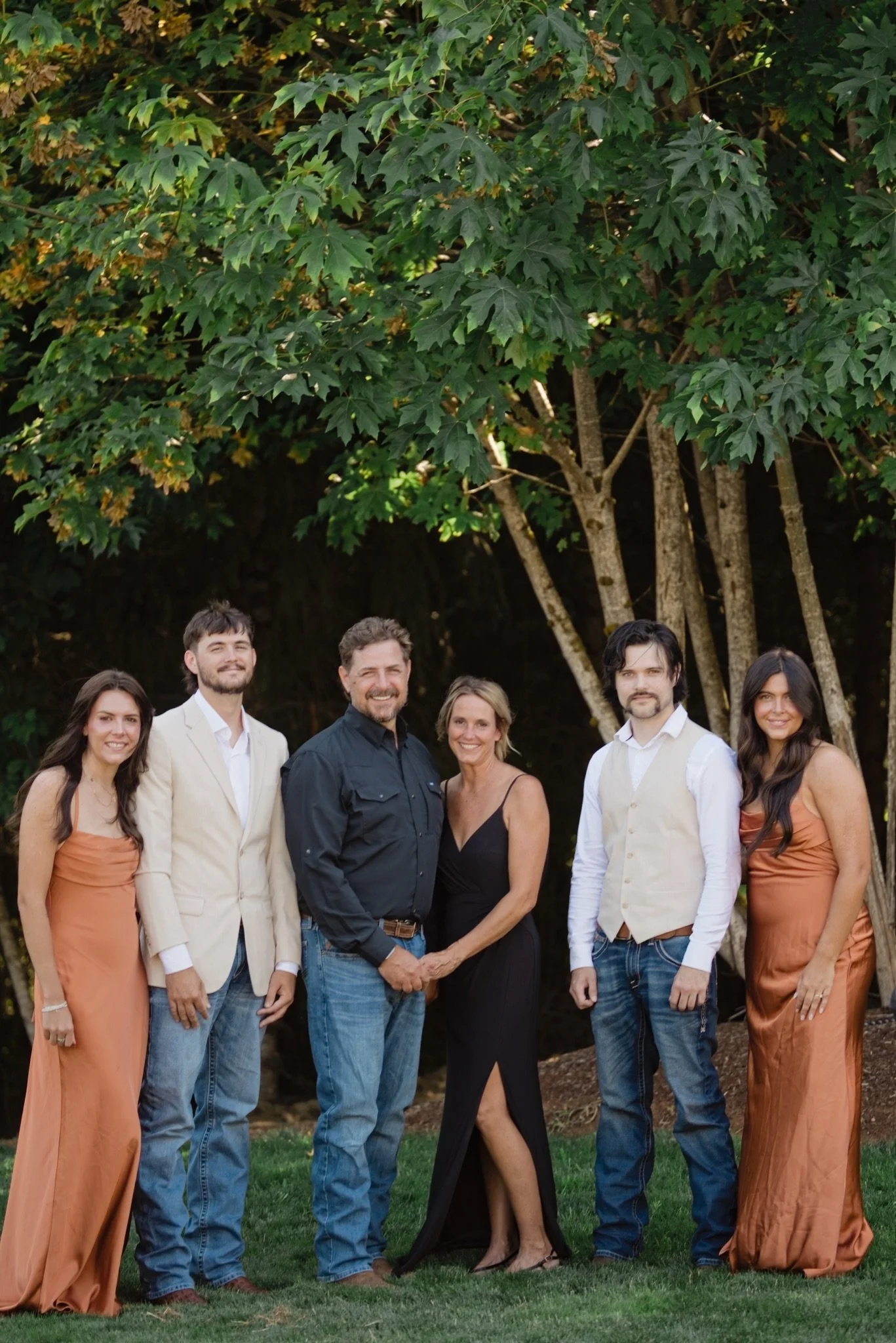 Reed with the wedding party in rust and black in front of the trees