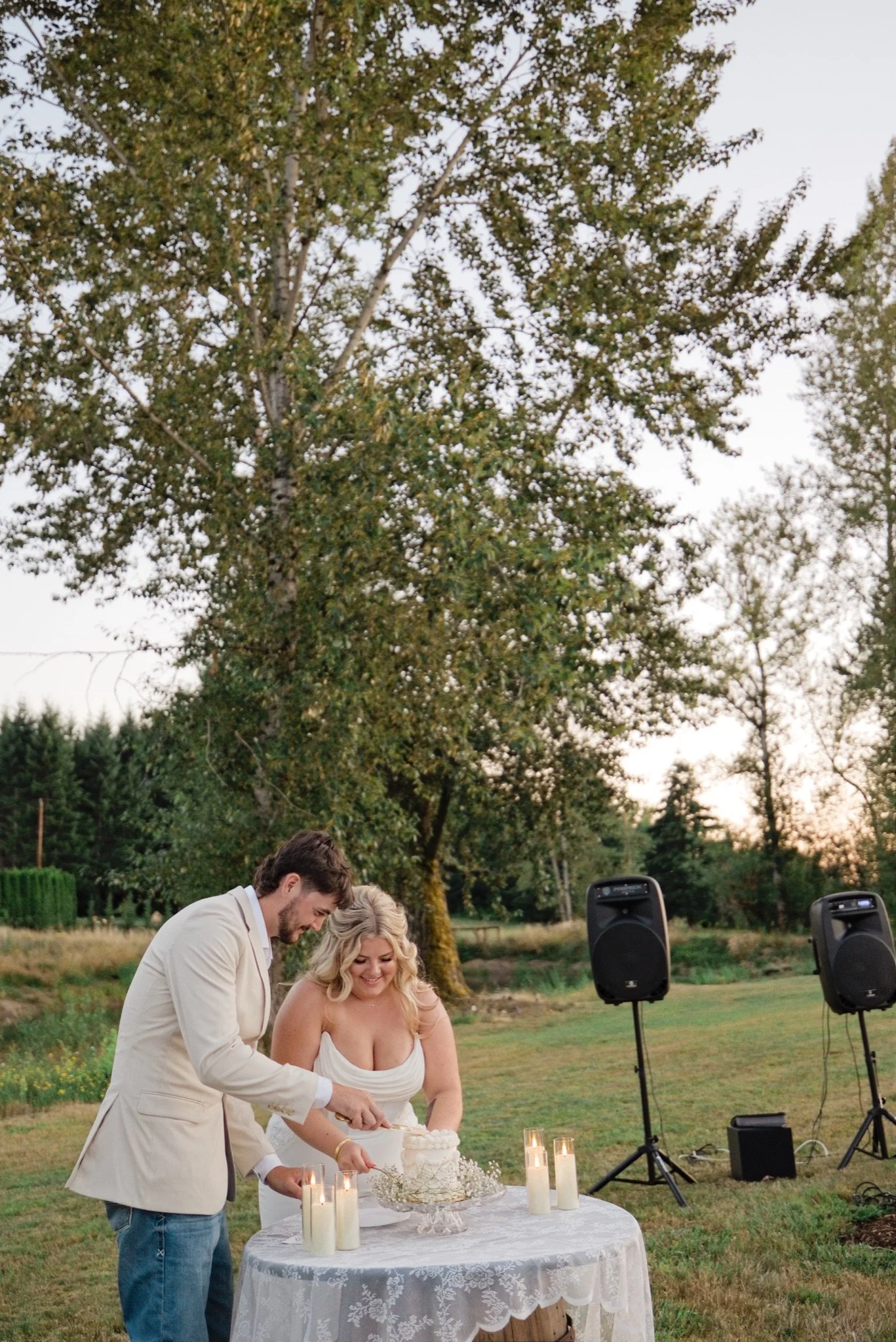 Sarah and Reed cutting their cake under the trees