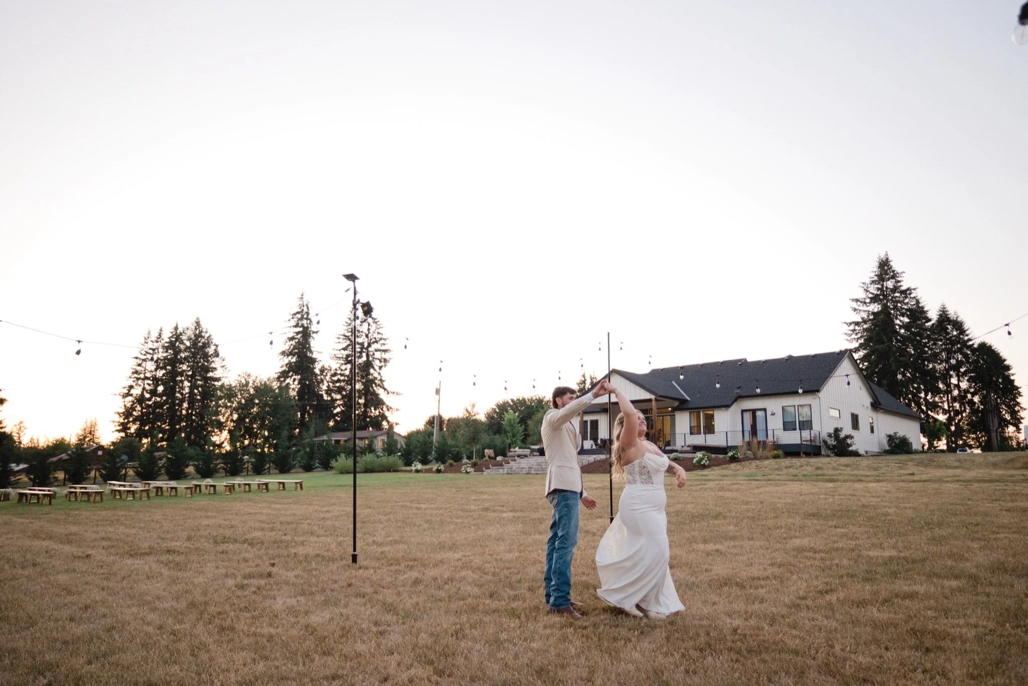 Sarah and Reed under the string lights at the farmhouse at dusk