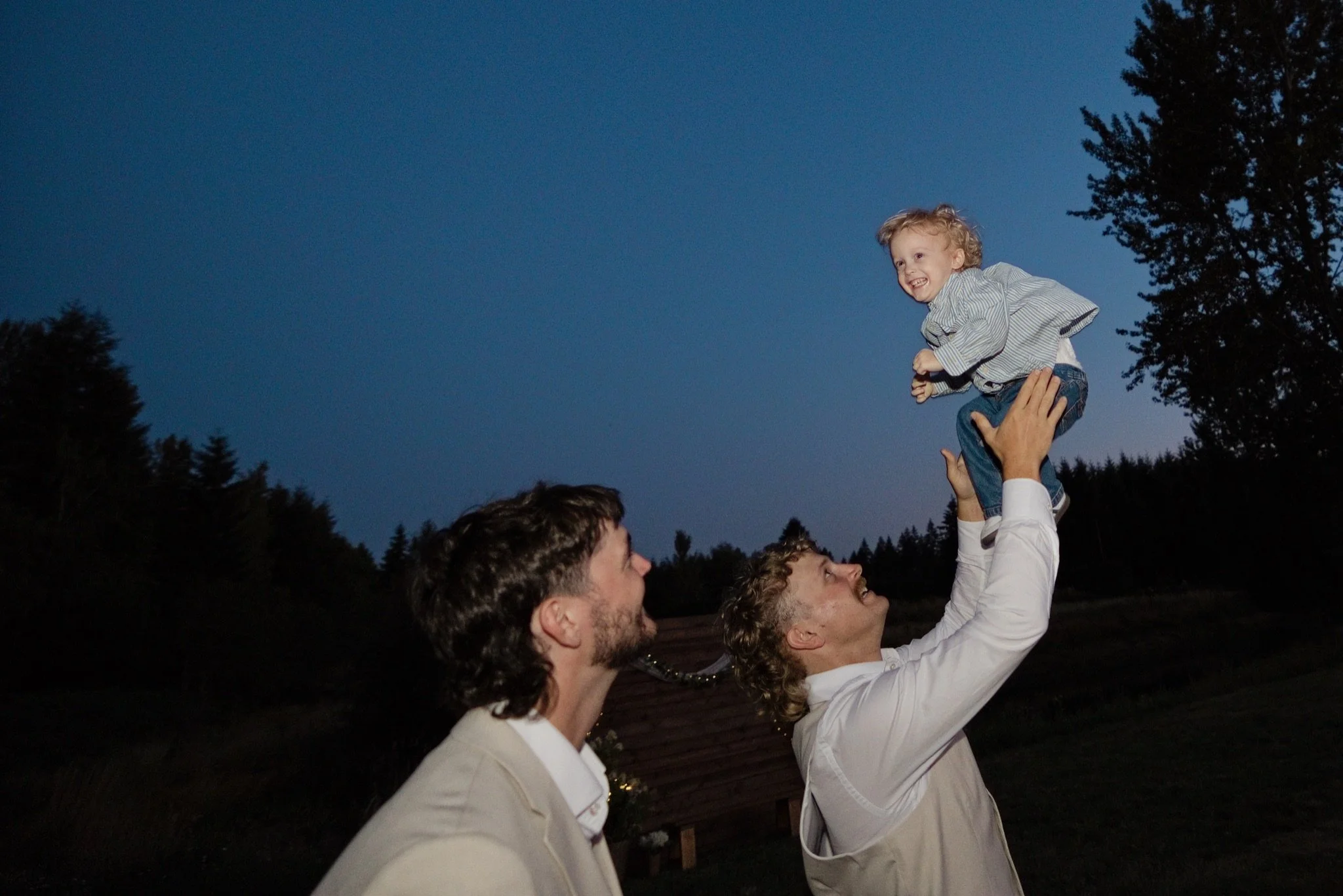 Reed lifting their little boy into the air at twilight