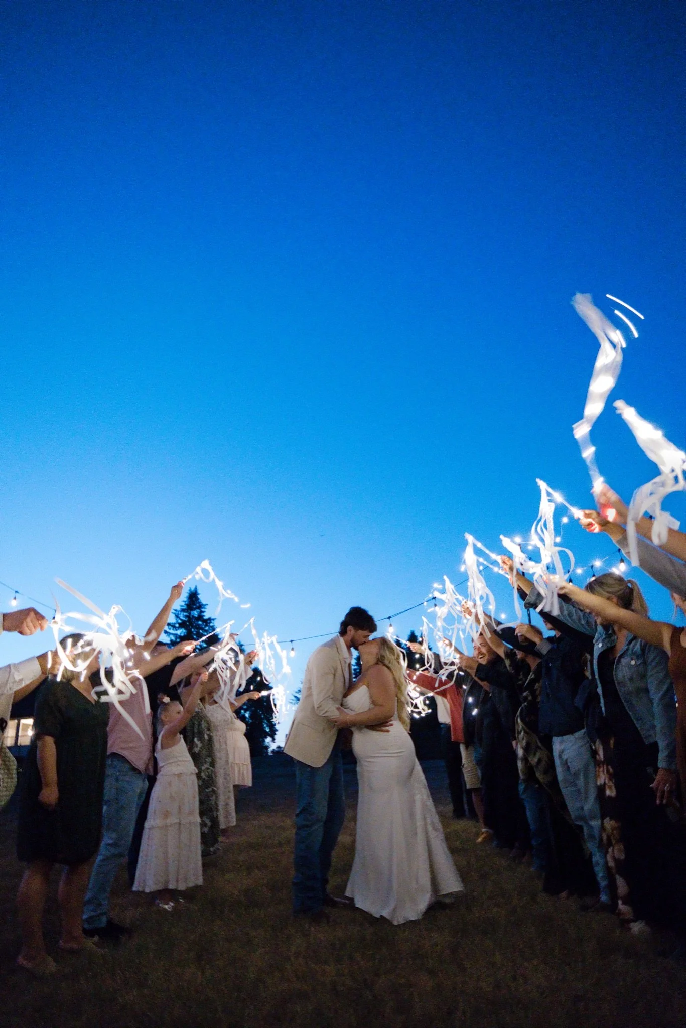 Sarah and Reed running through the ribbon wand send off under a blue dusk sky