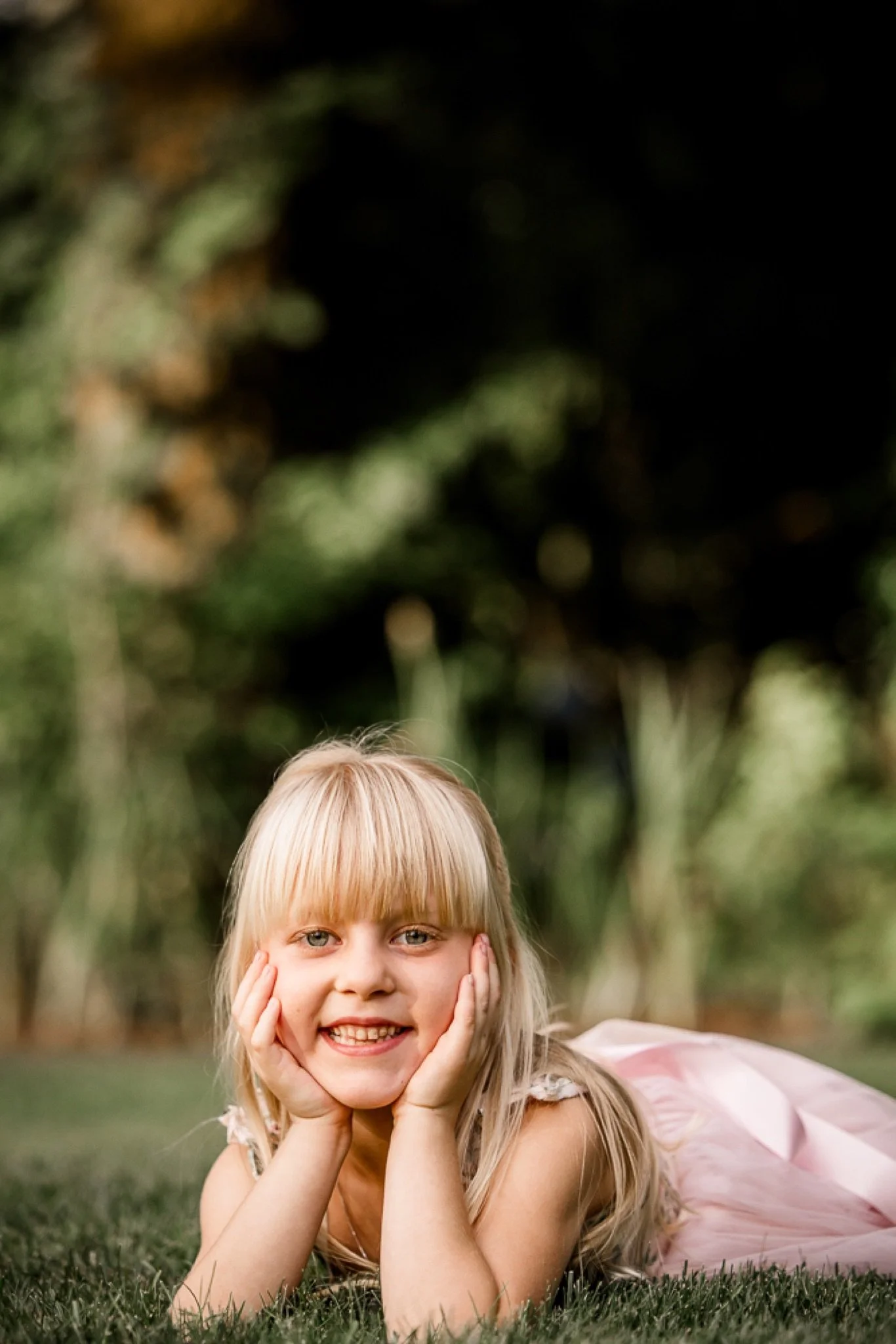 A little girl in pink lying in the grass with her chin in her hands