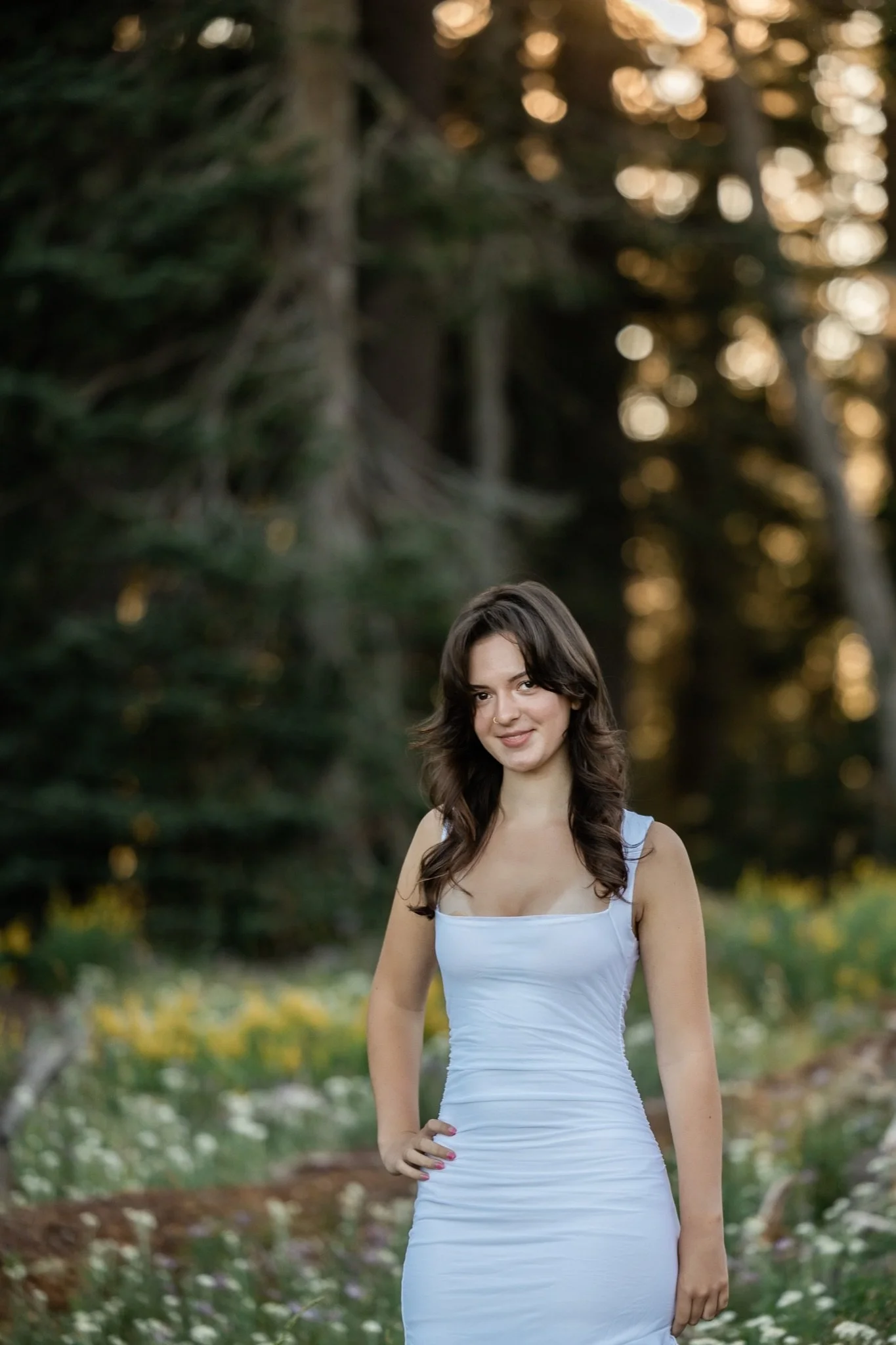 Hailey smiling in the meadow with the sun through the firs behind her