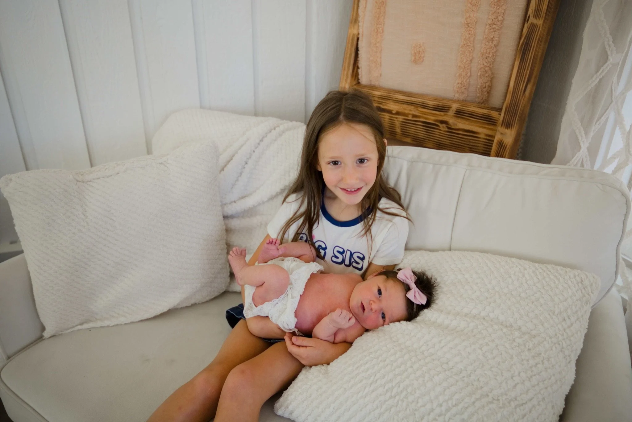 Big sister holding newborn Stevie on the white couch