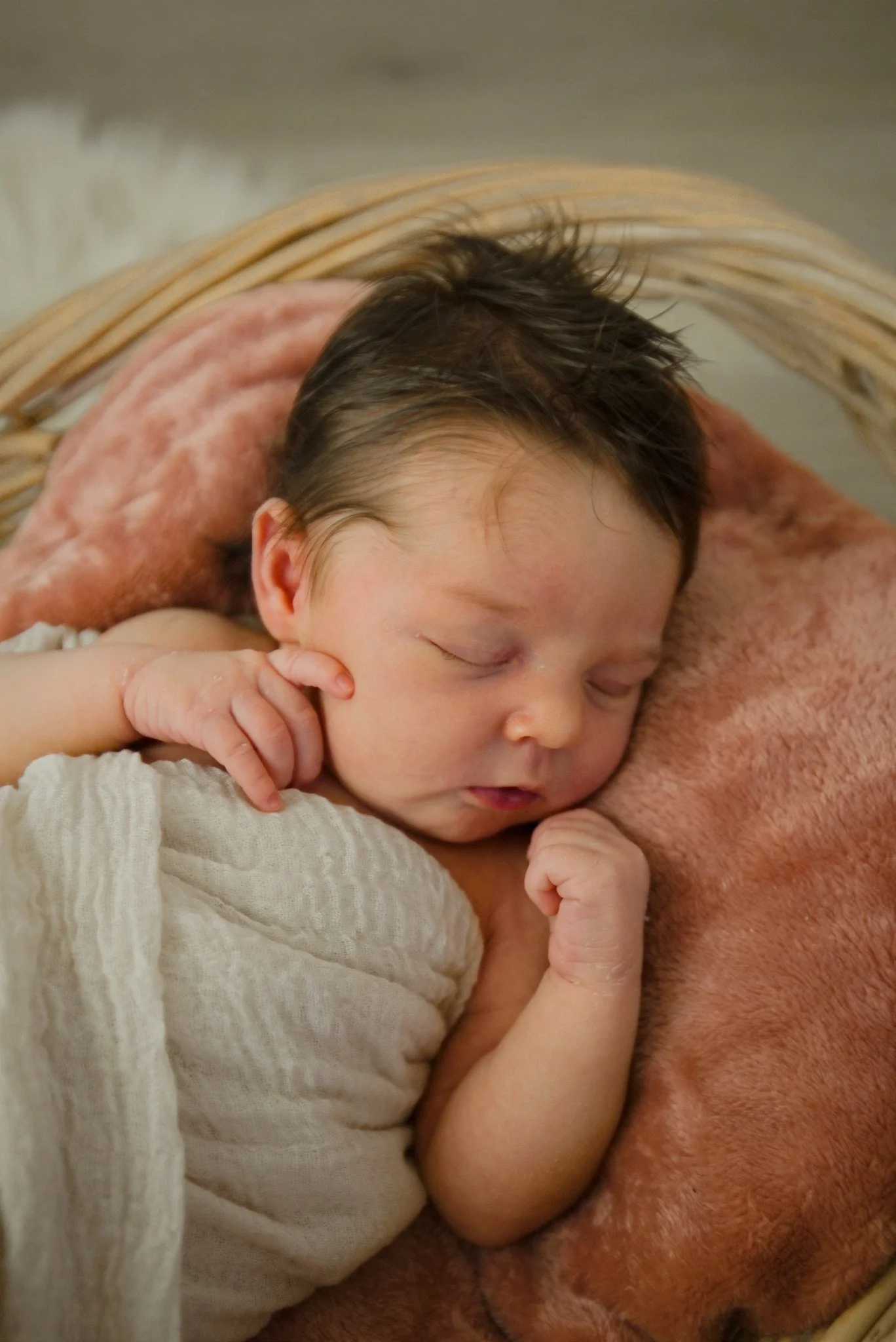 Newborn Stevie wrapped in cream in a wicker basket
