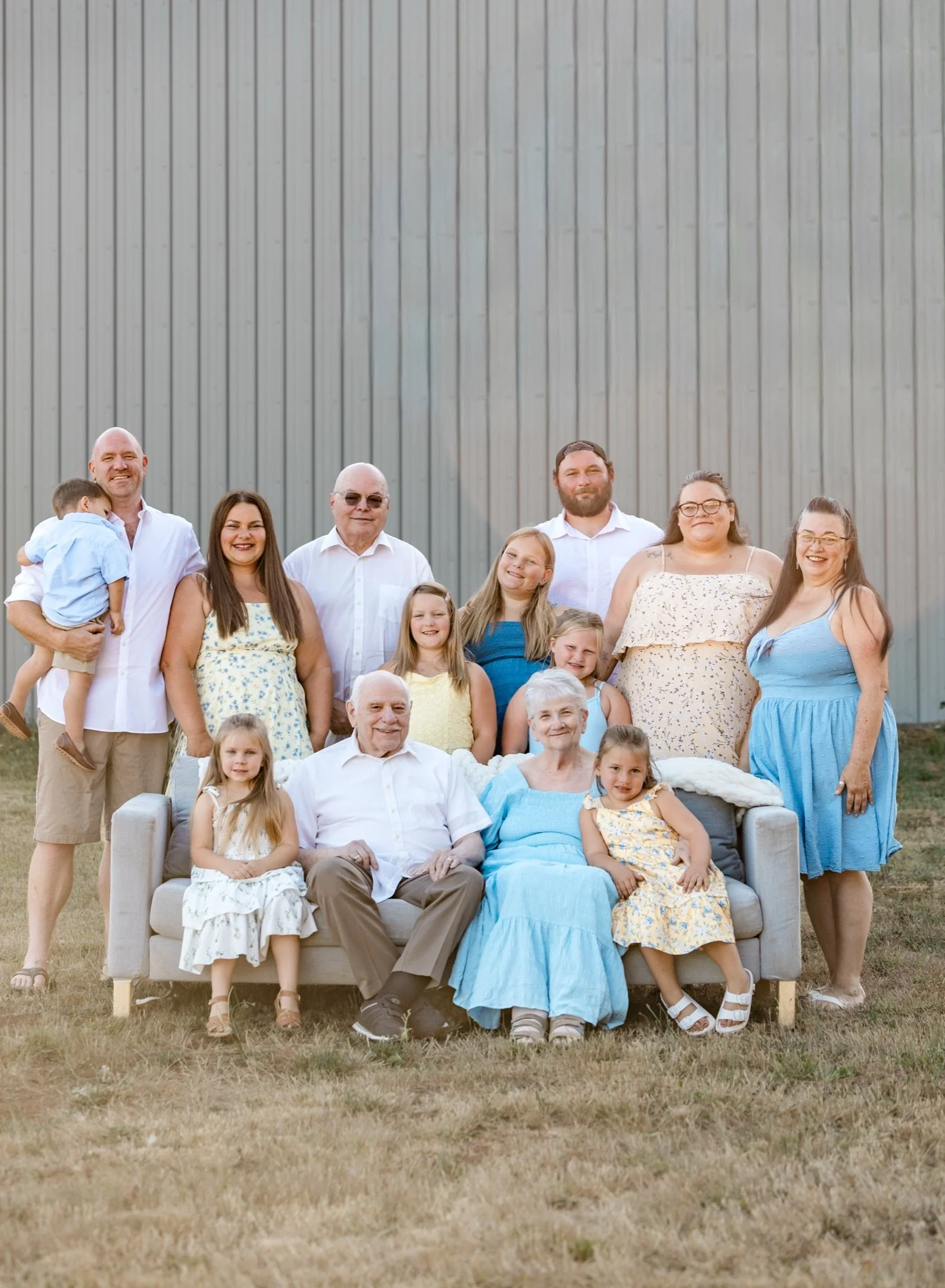 The whole extended family in yellow and blue gathered on a gray couch in a summer field near Sandy Oregon