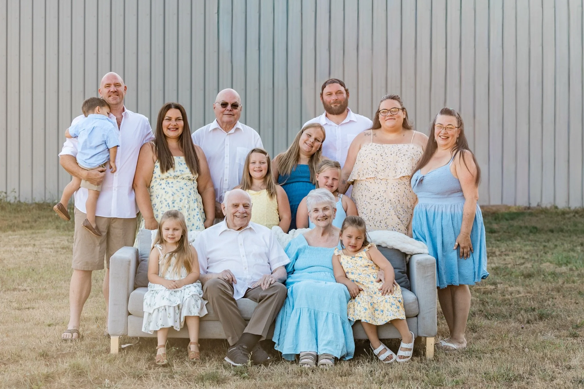 Three generations in yellow and blue around the couch in the dry grass, extended family session