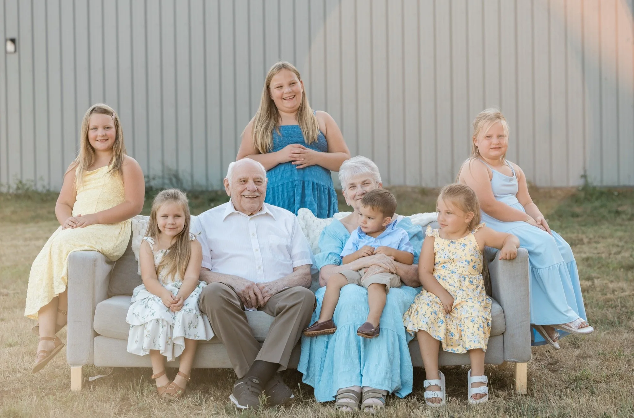 The extended family seated on a gray couch in the golden evening grass with Mt. Hood on the horizon