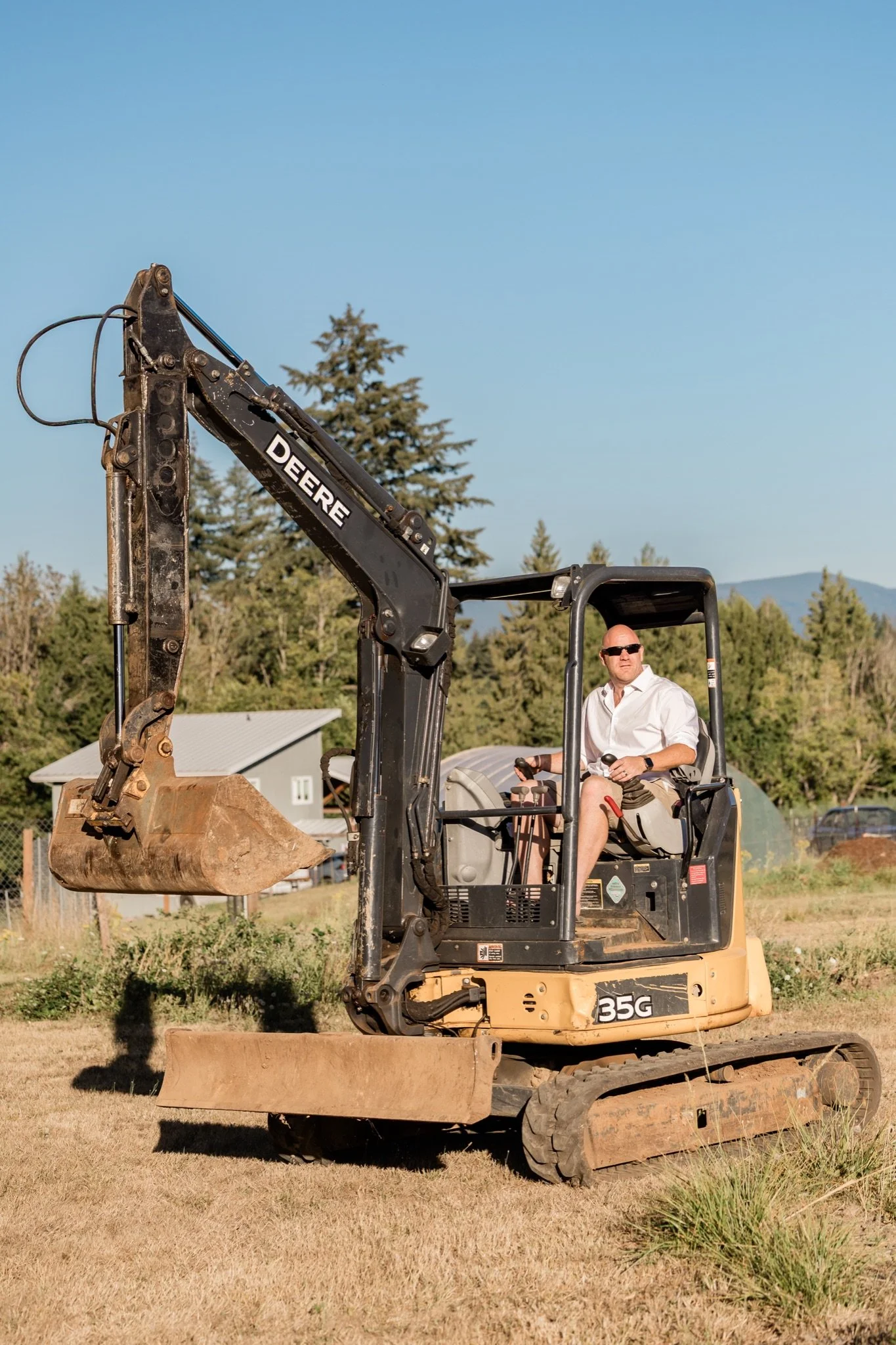 A little boy in blue sitting on a yellow excavator in the field at golden hour