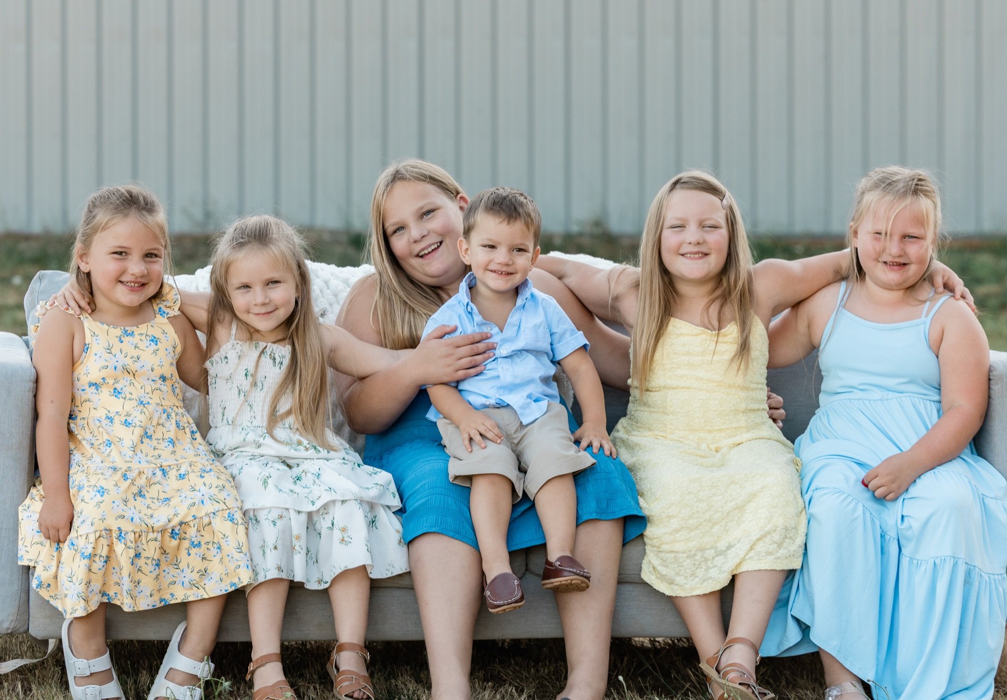 Cousins in yellow and blue piled together on the couch in the summer grass