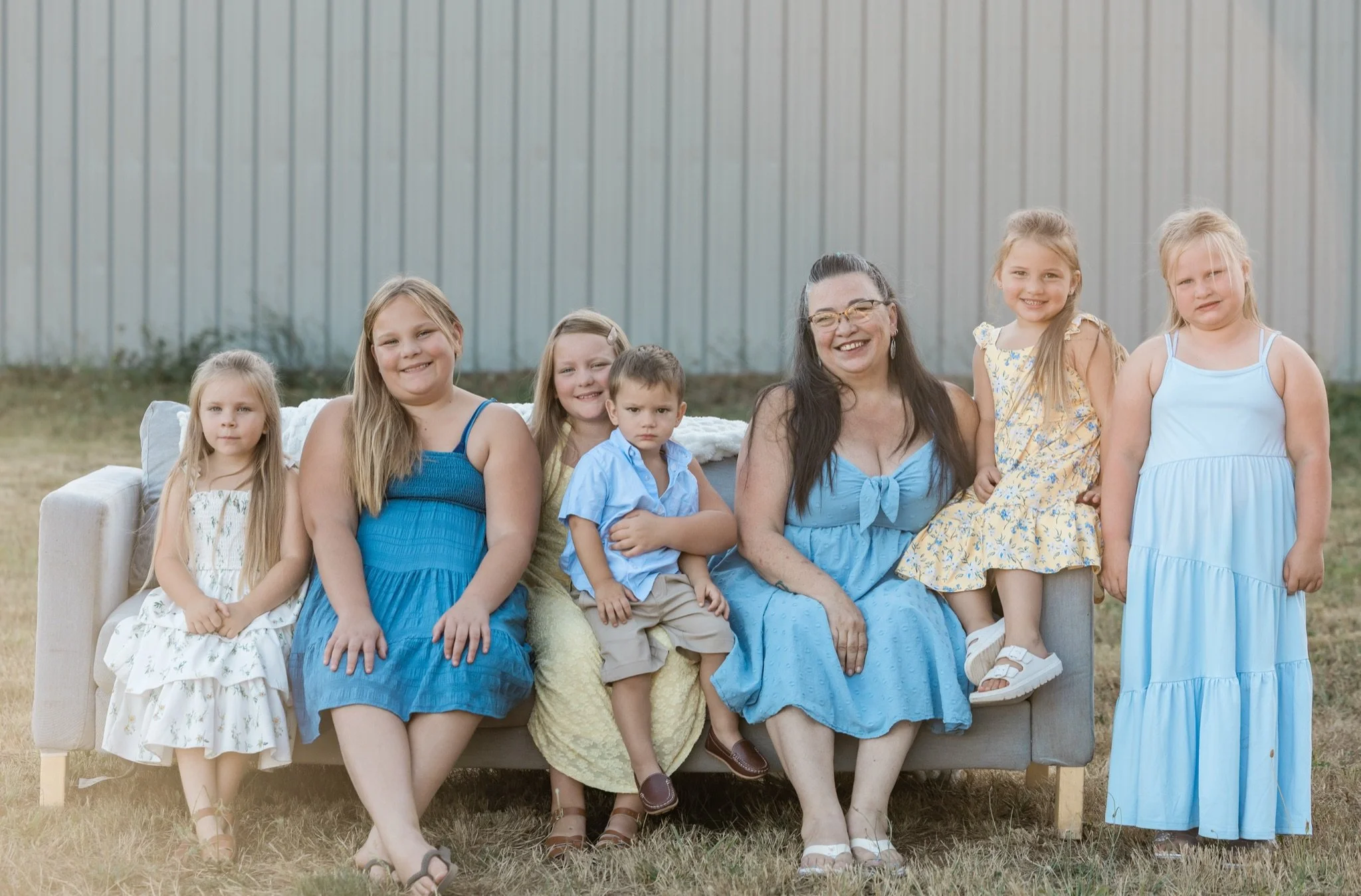 Three sisters in yellow and blue dresses on the couch in the field