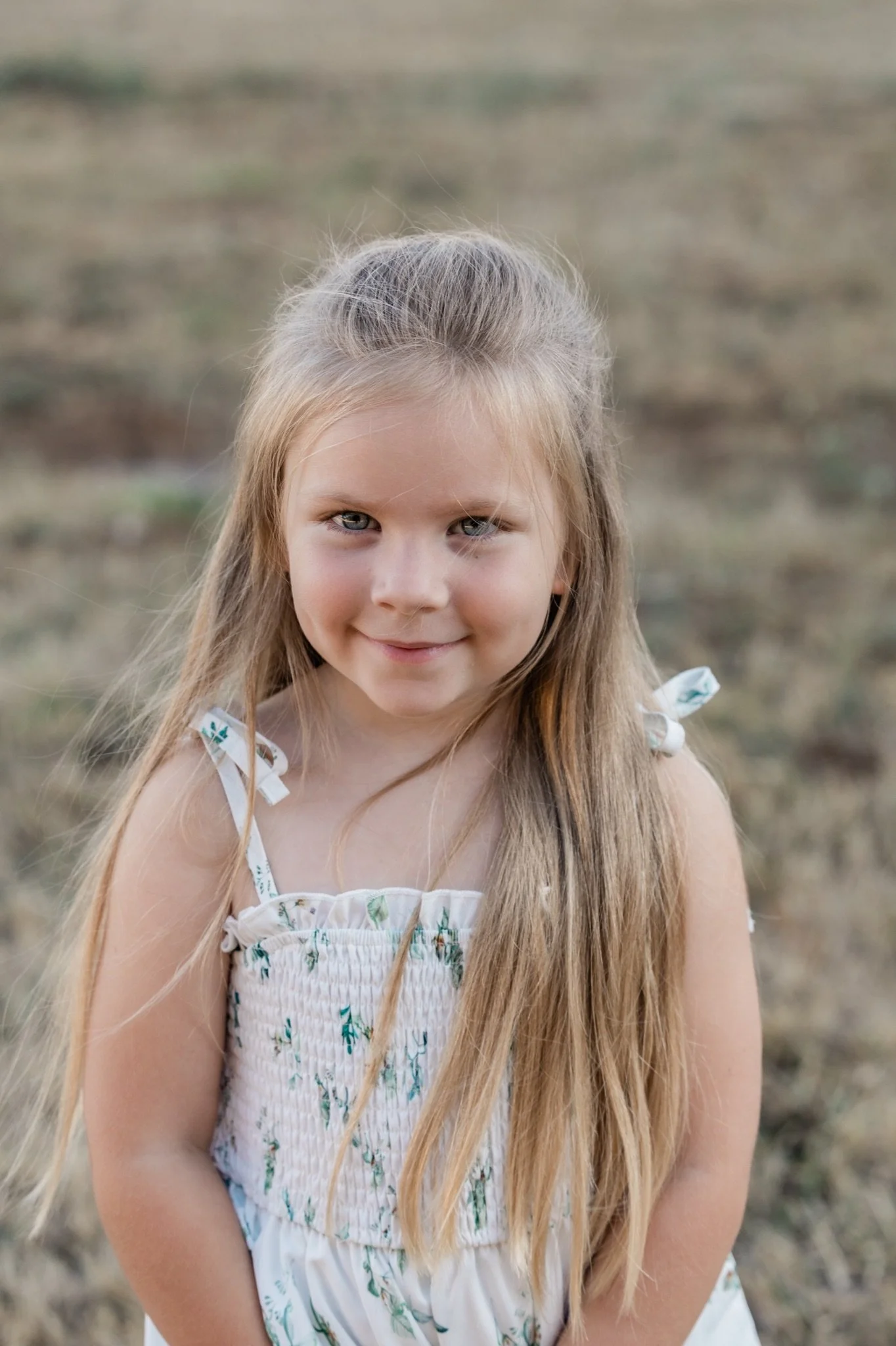 A little girl in a floral sundress smiling in the golden grass