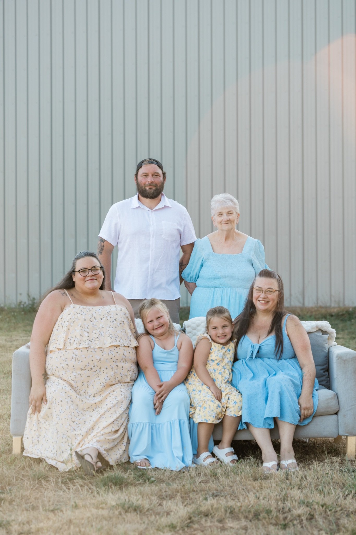 Mom, dad and their girls on the couch in the field with the corrugated barn behind them