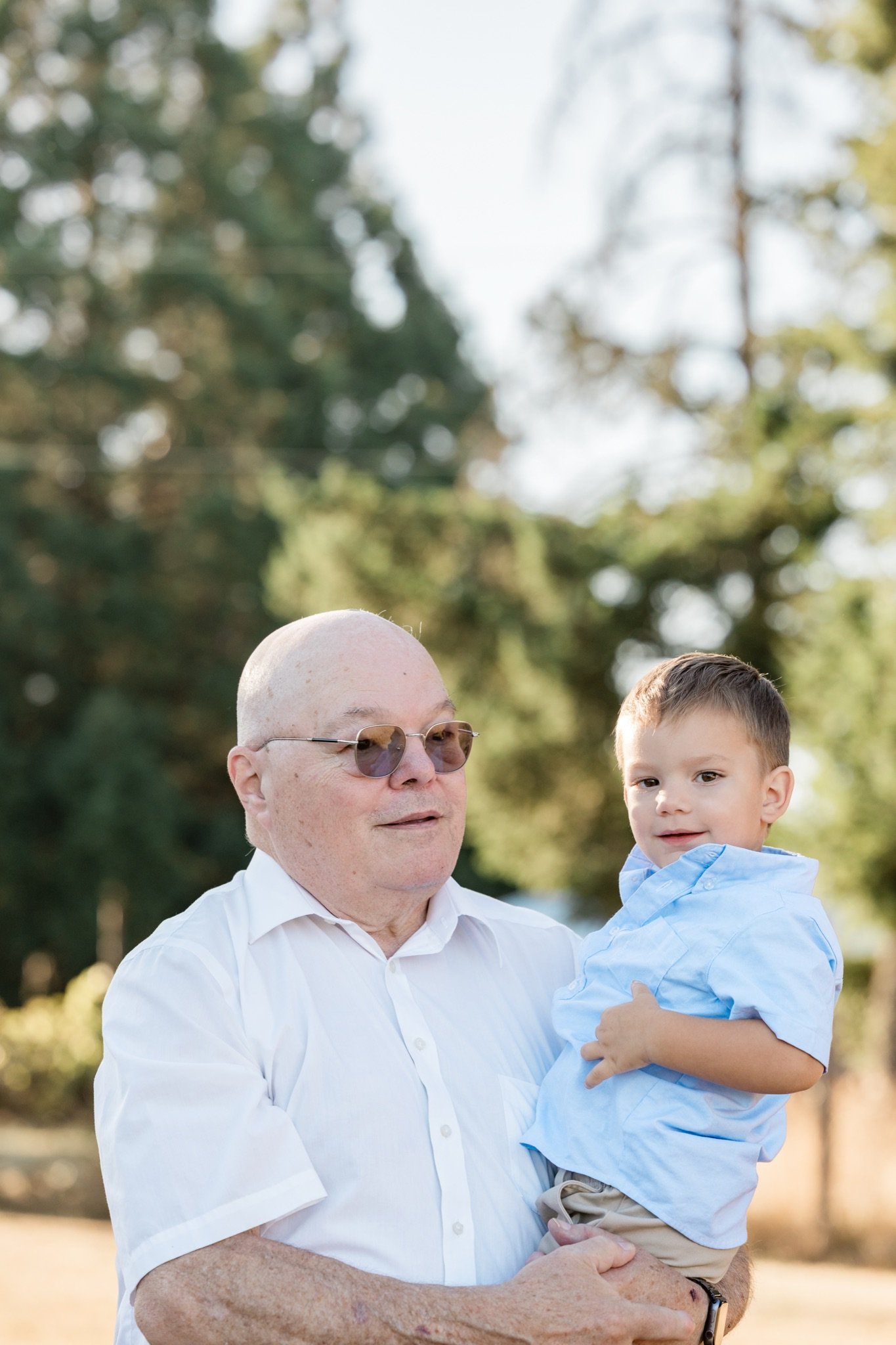 Grandpa holding his grandson under the trees at golden hour