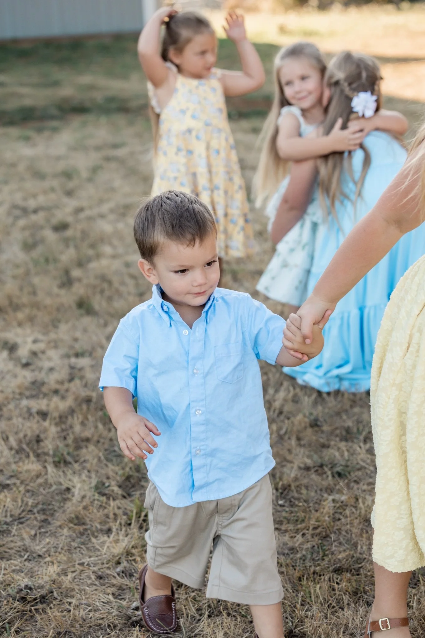 A little boy in a blue shirt holding hands with his sisters in the grass