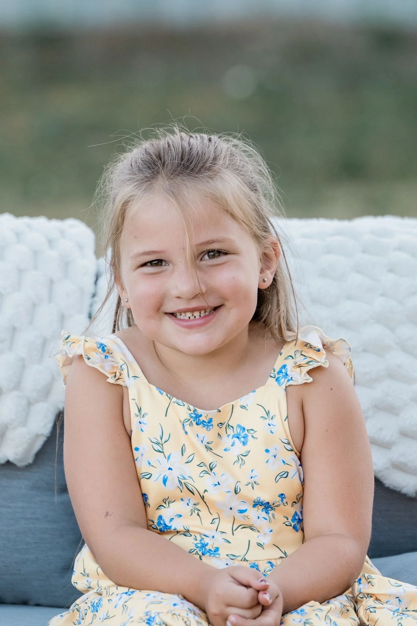 A little girl in a yellow floral dress sitting on the couch