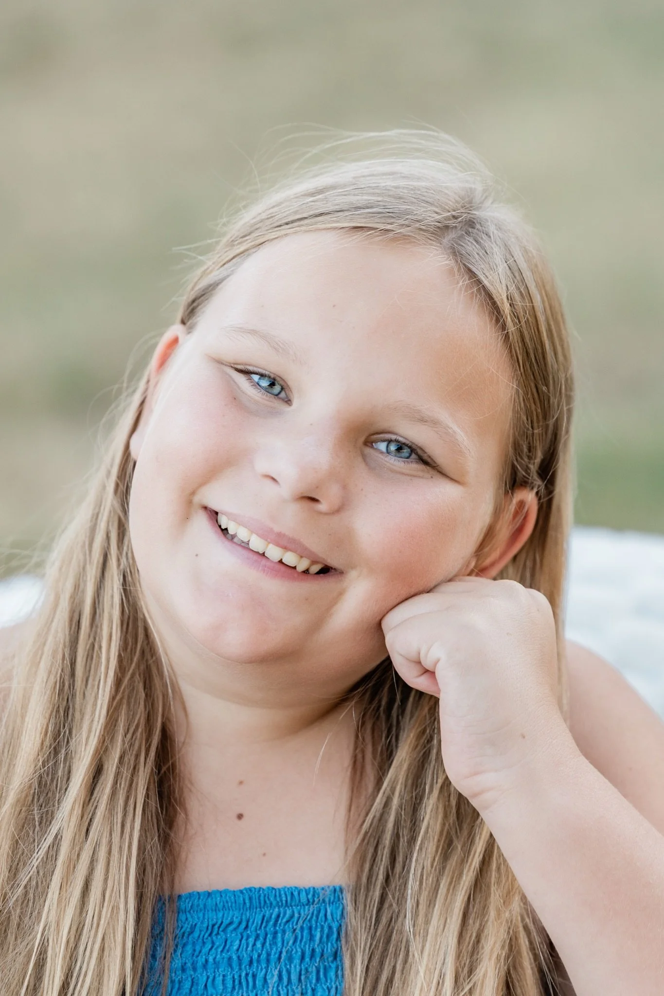 A girl in a blue dress resting her chin on her hand at golden hour