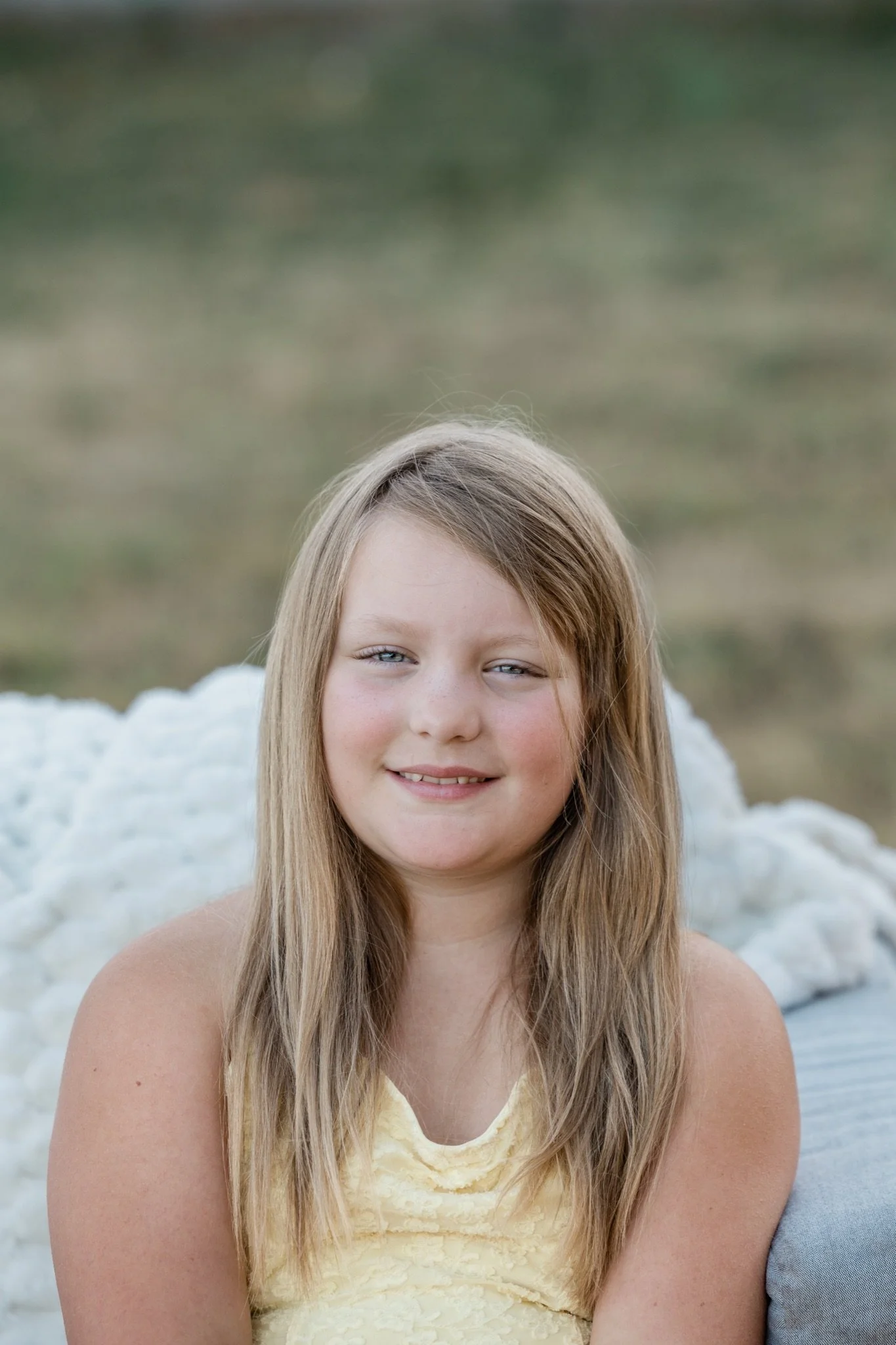 A girl in a yellow dress sitting on the couch in the field