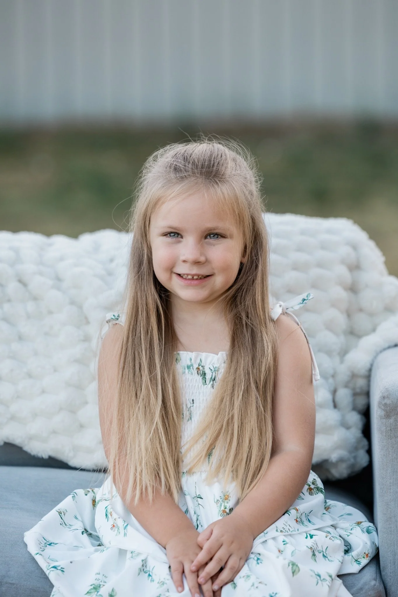 A little girl in a floral dress sitting on the couch with a white blanket