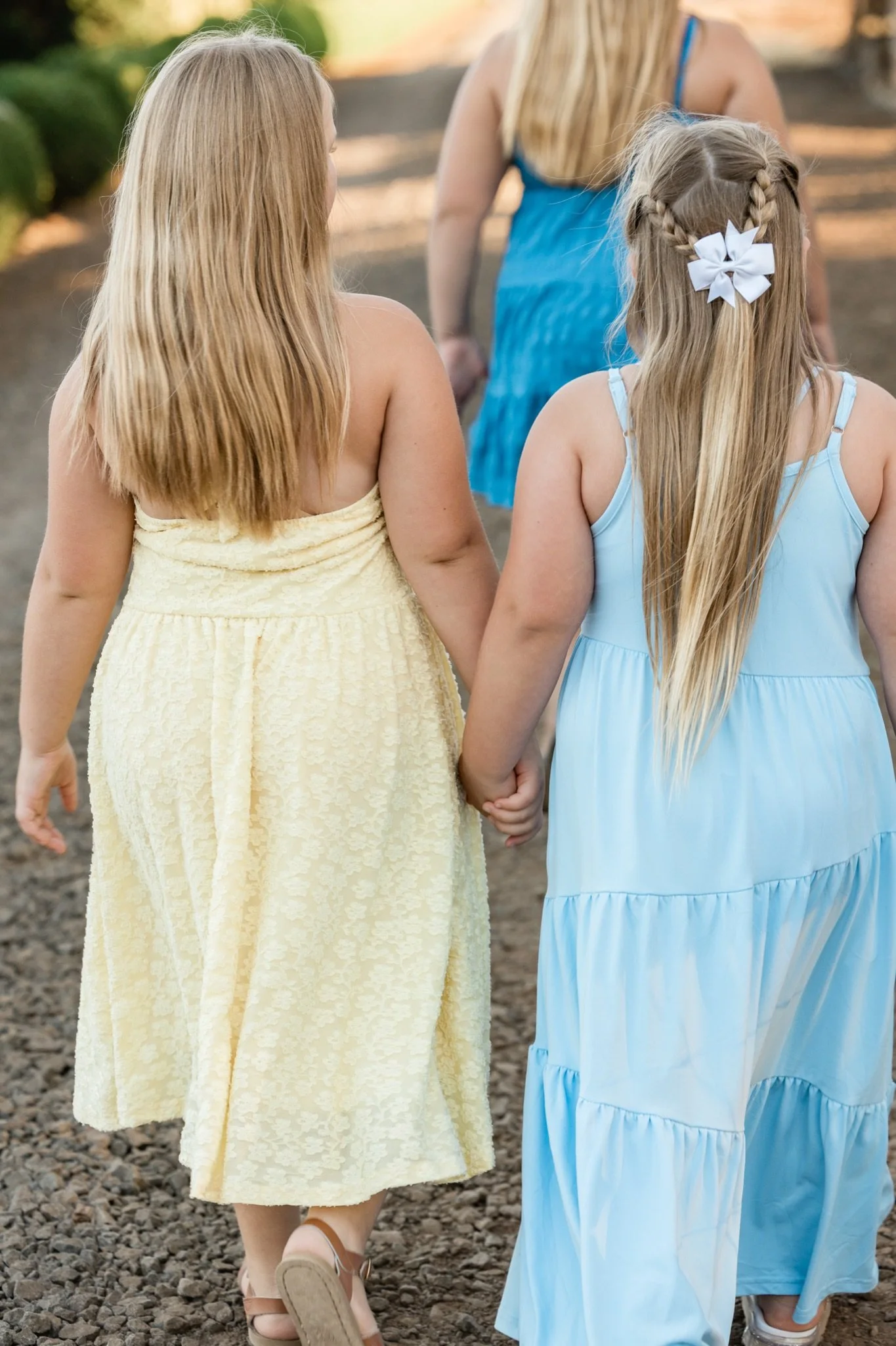 Two girls in yellow and blue dresses walking away through the grass