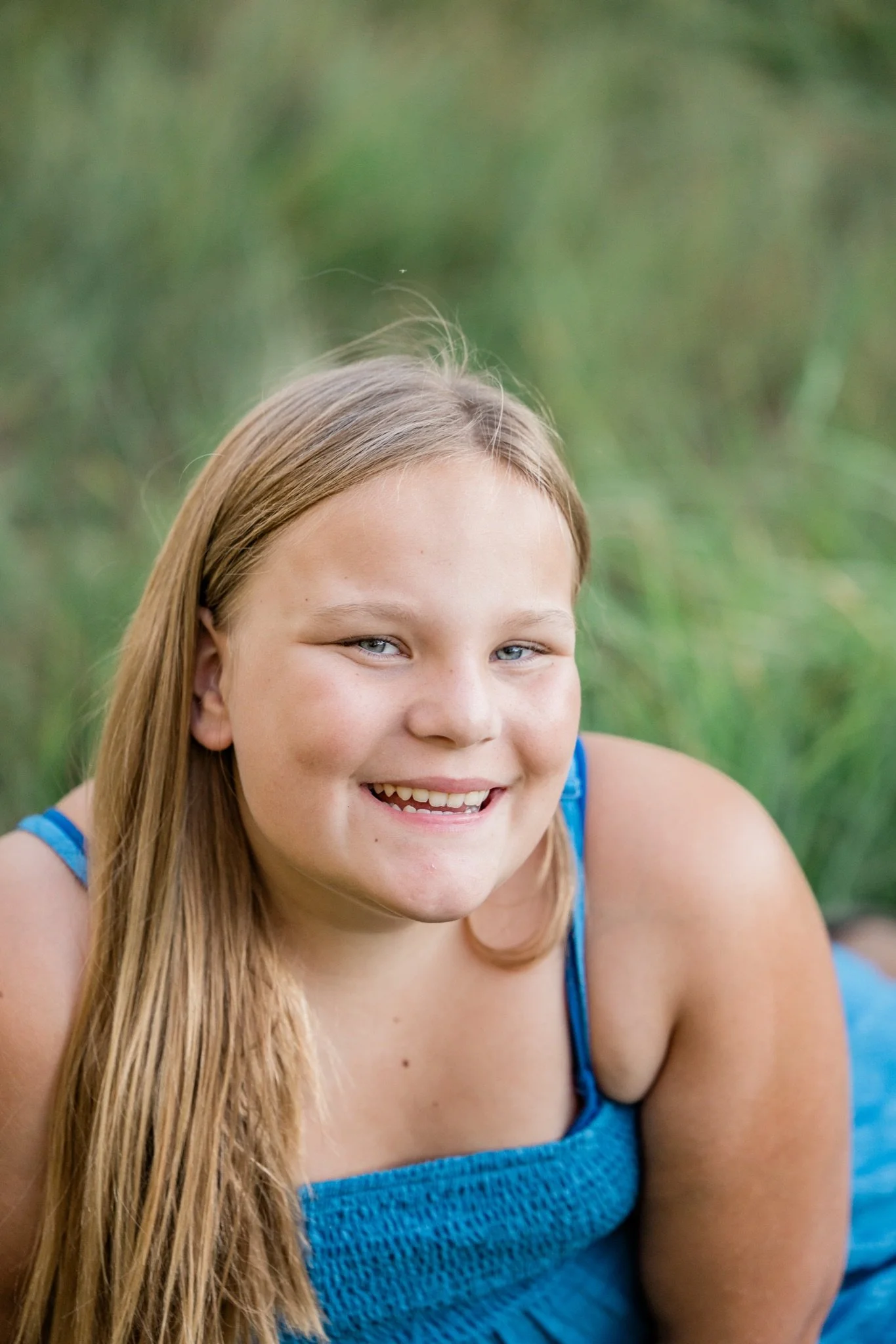A girl in a blue dress smiling in the tall green grass