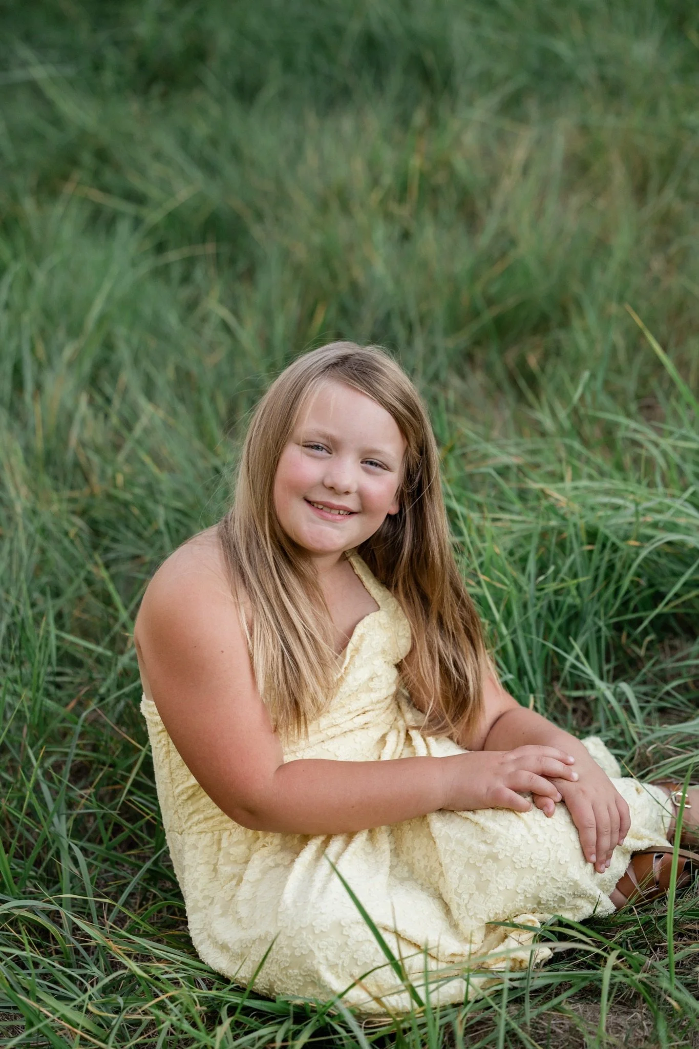 A girl in a yellow dress sitting in the tall grass at golden hour
