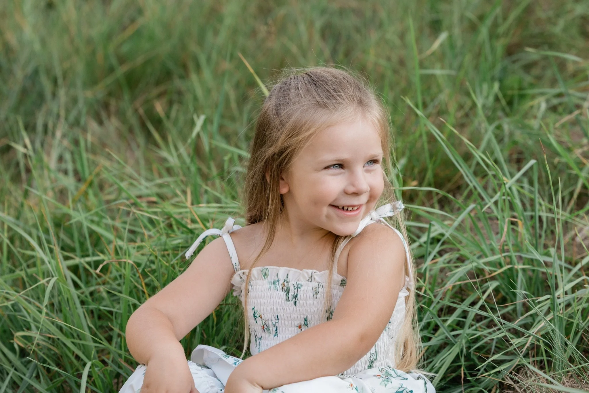 A little girl in a floral sundress laughing in the tall grass