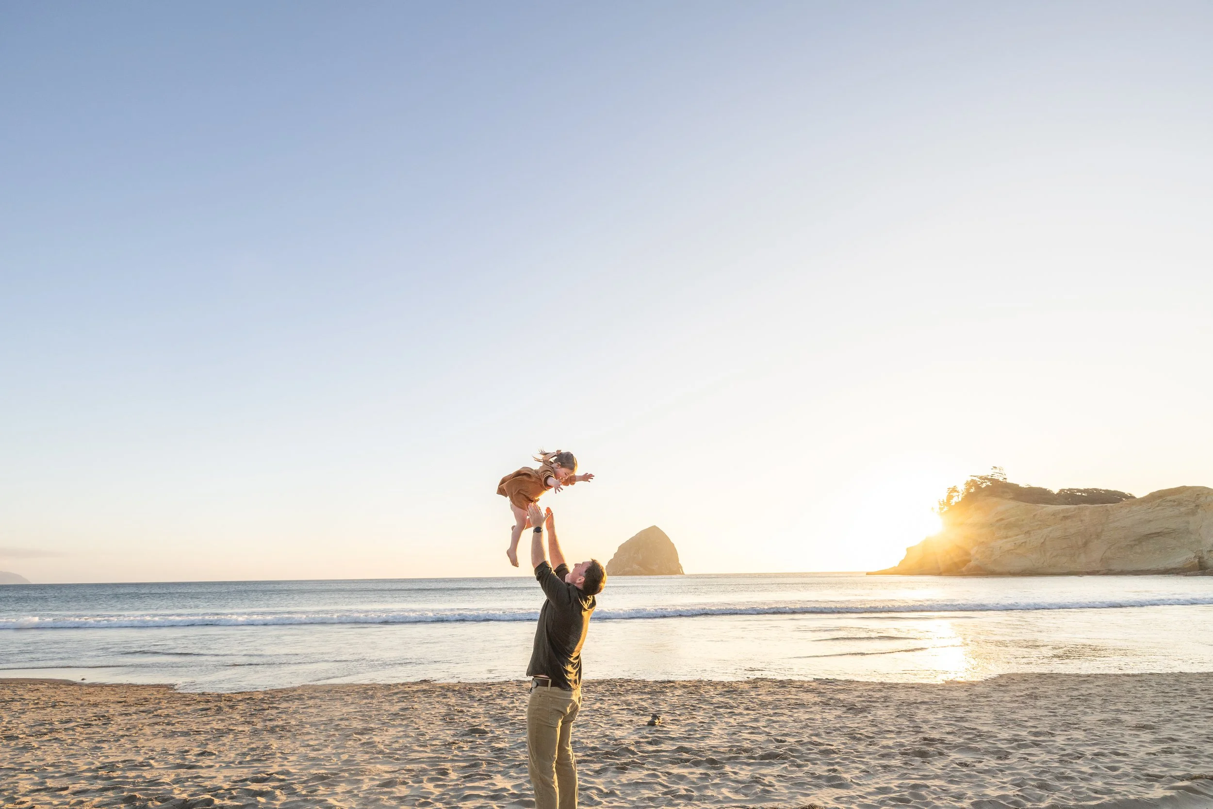 Toddler toss at the water's edge as the sun drops behind the cape, by a Cape Kiwanda family photographer