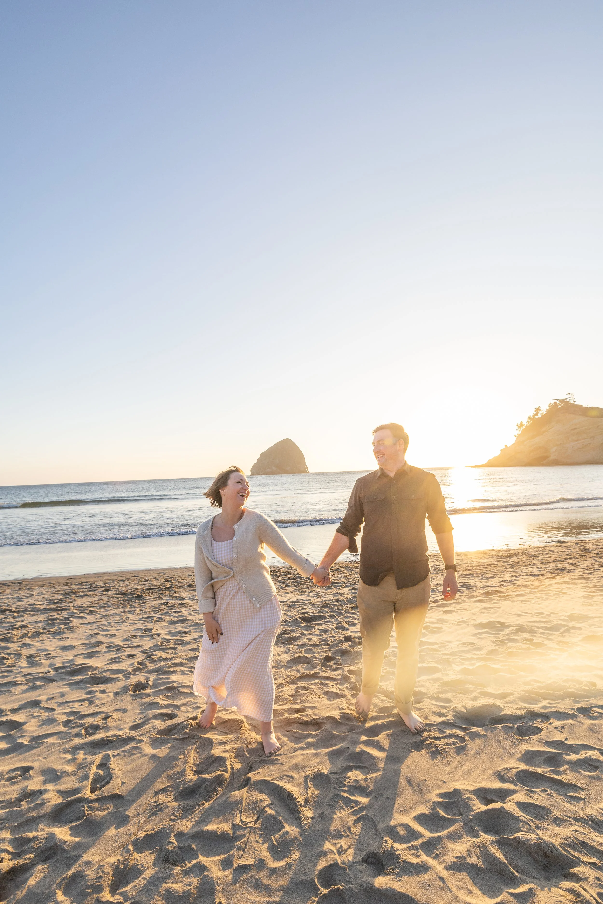 Mom and dad hold hands walking up the beach from the surf with Haystack Rock behind them