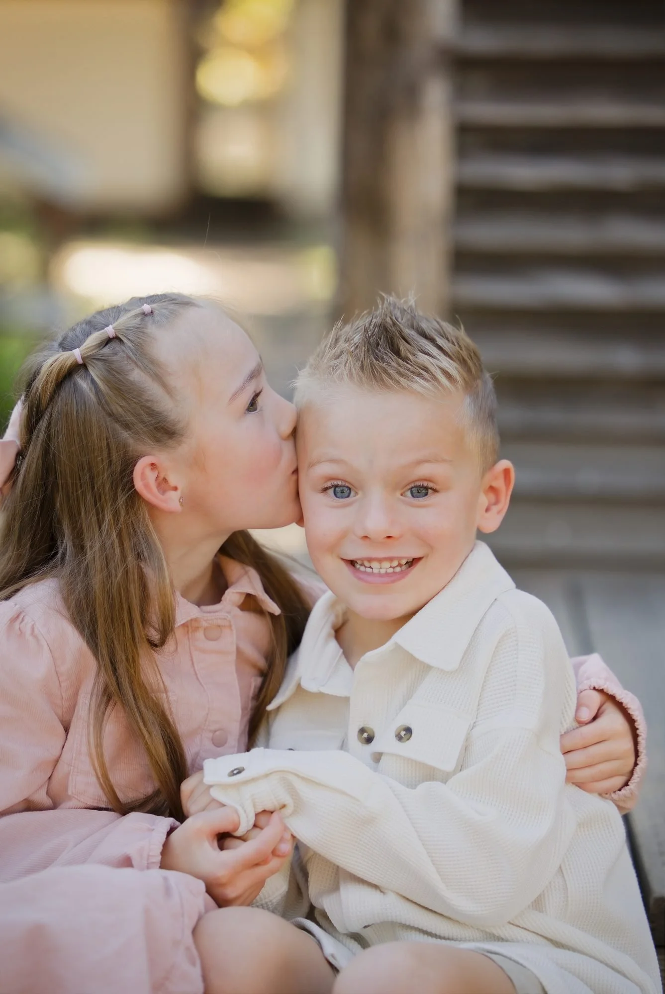Big sister kissing her little brother on the cheek on the farmhouse steps at golden hour
